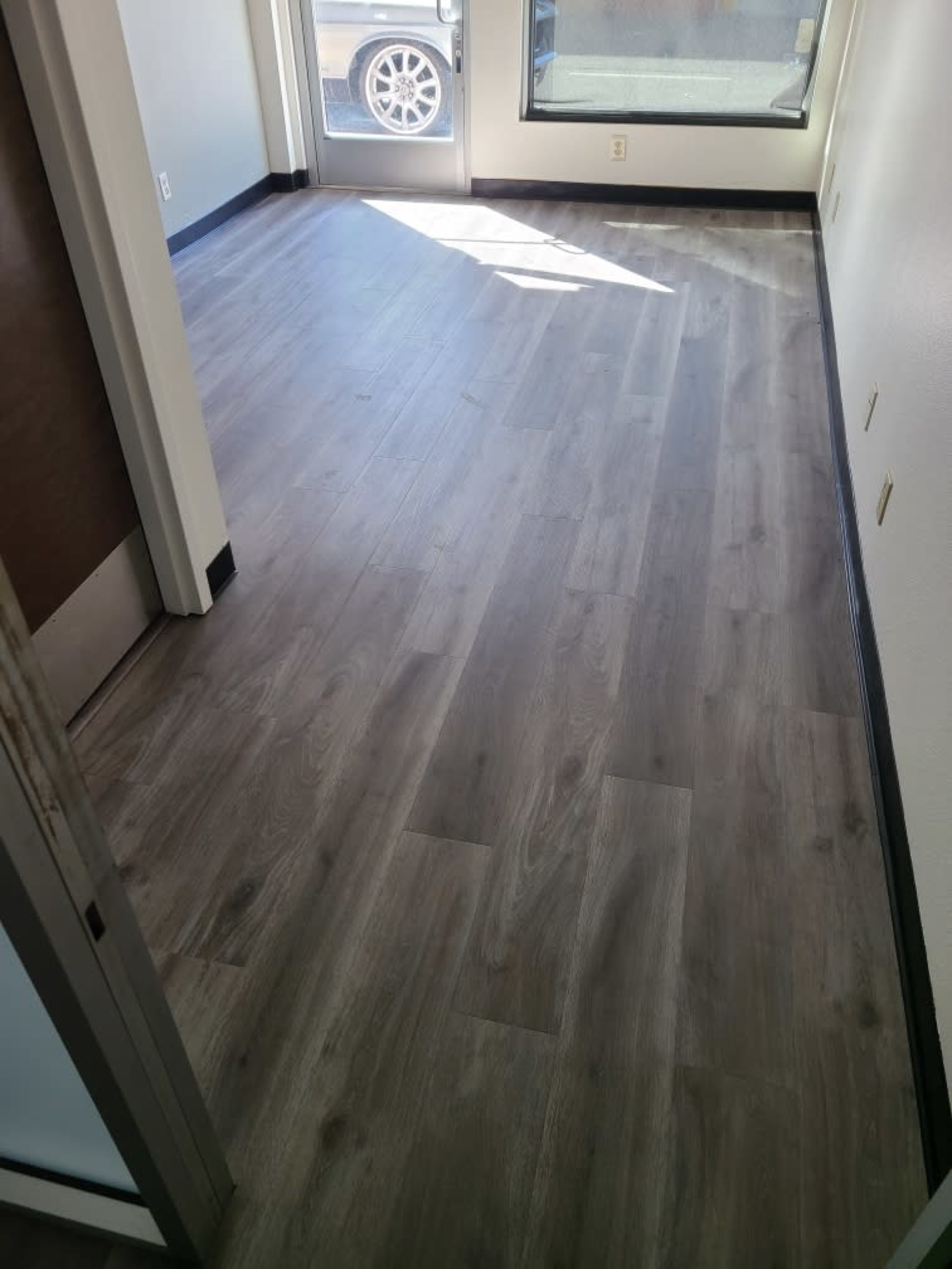 A light-colored, wooden floor in a bright room with large windows and a door leading outside.