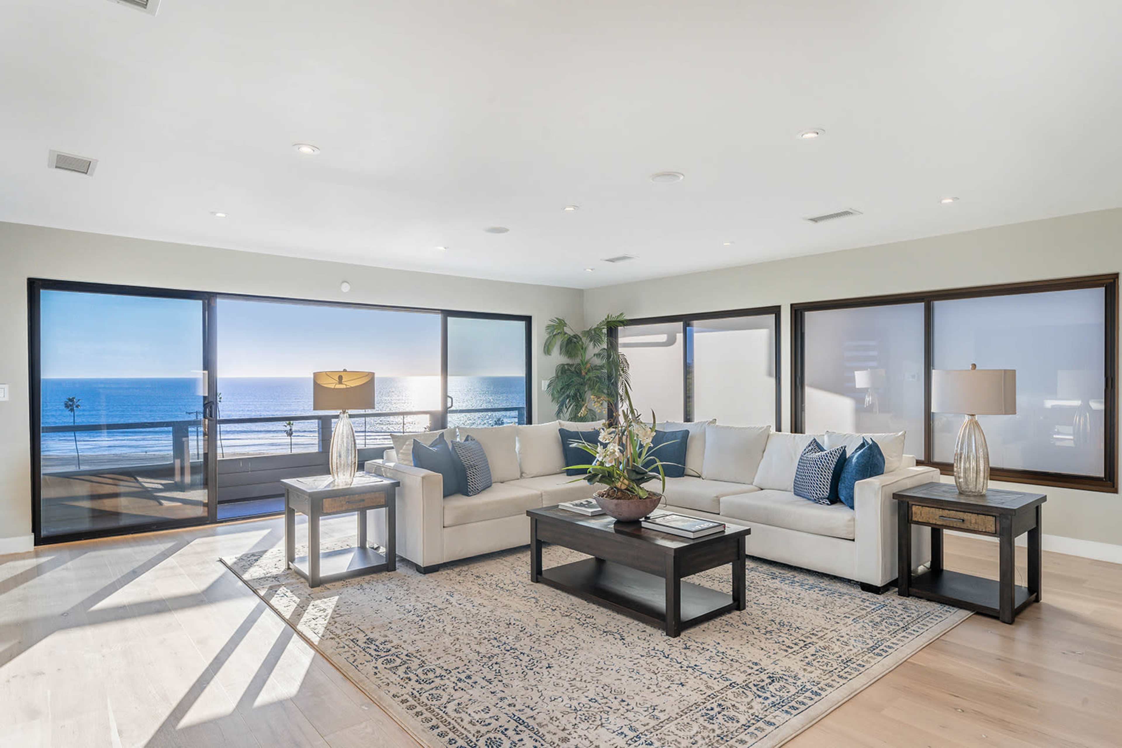 A modern living room with a light-colored sofa, a wooden coffee table, and large windows overlooking an ocean view.