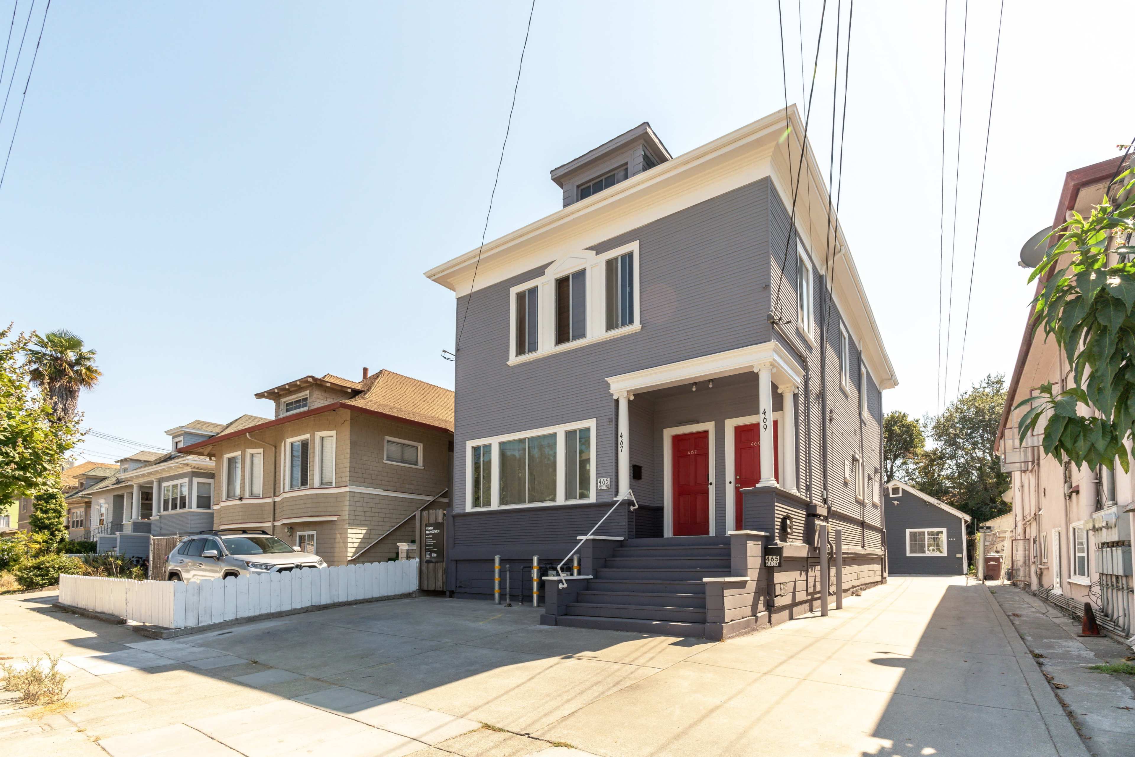 A two-story house with gray siding and red doors, located on a street lined with other residential buildings.