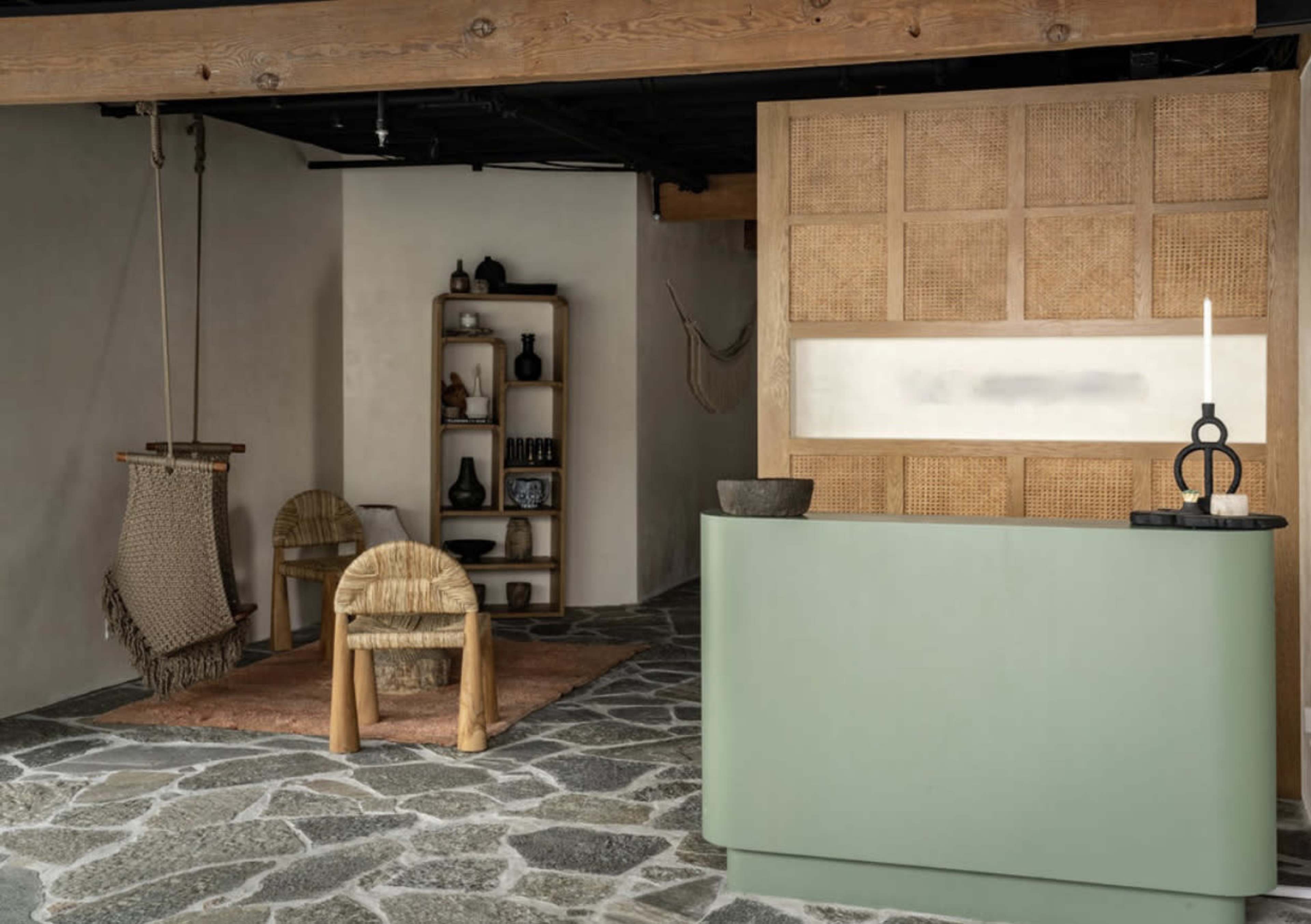 A modern interior space featuring a green reception desk, a textured wall, a swing chair, and a bookshelf with decorative items.