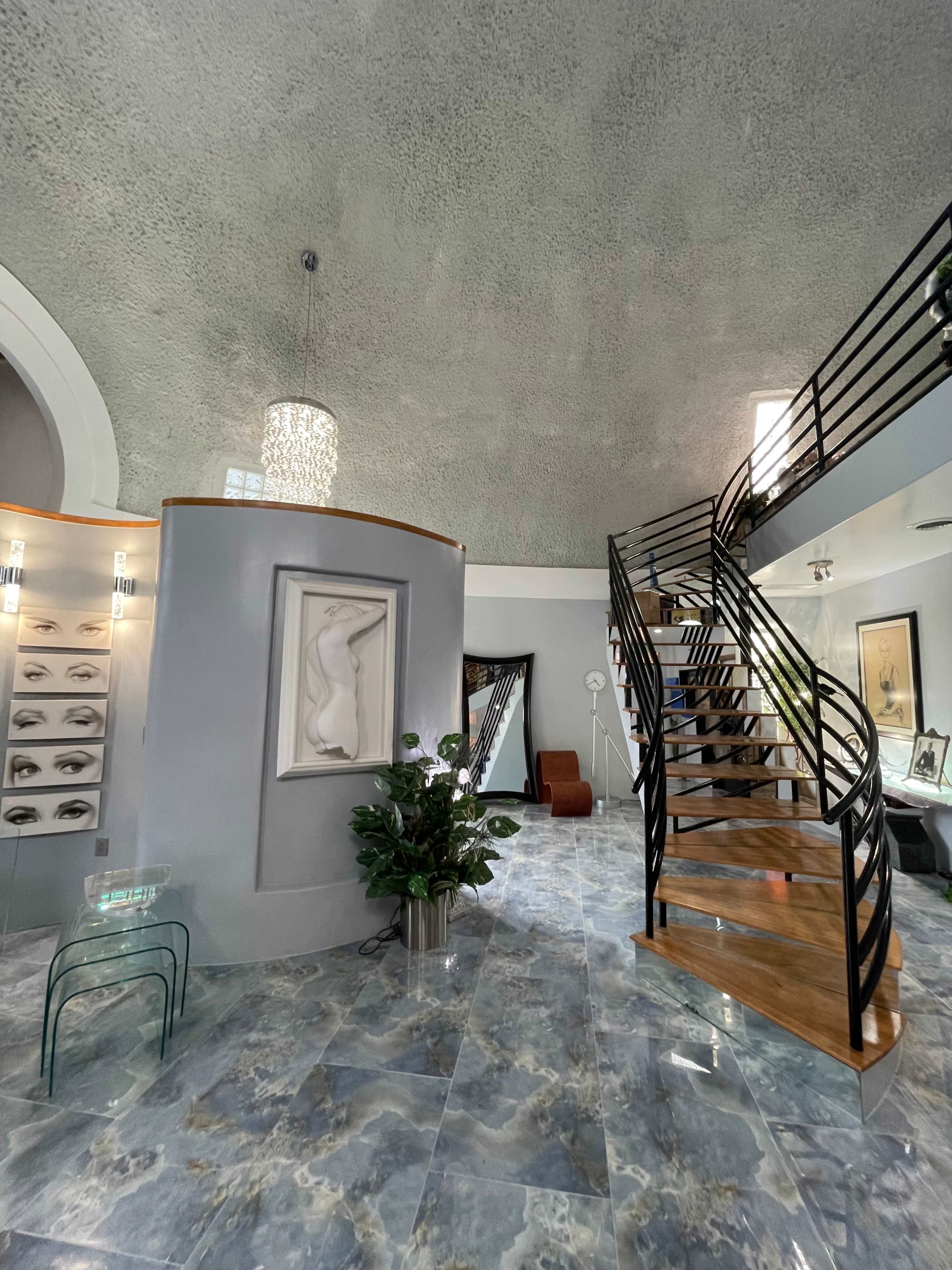 A modern entryway with a curved wall, a wooden staircase, and decorative artwork.