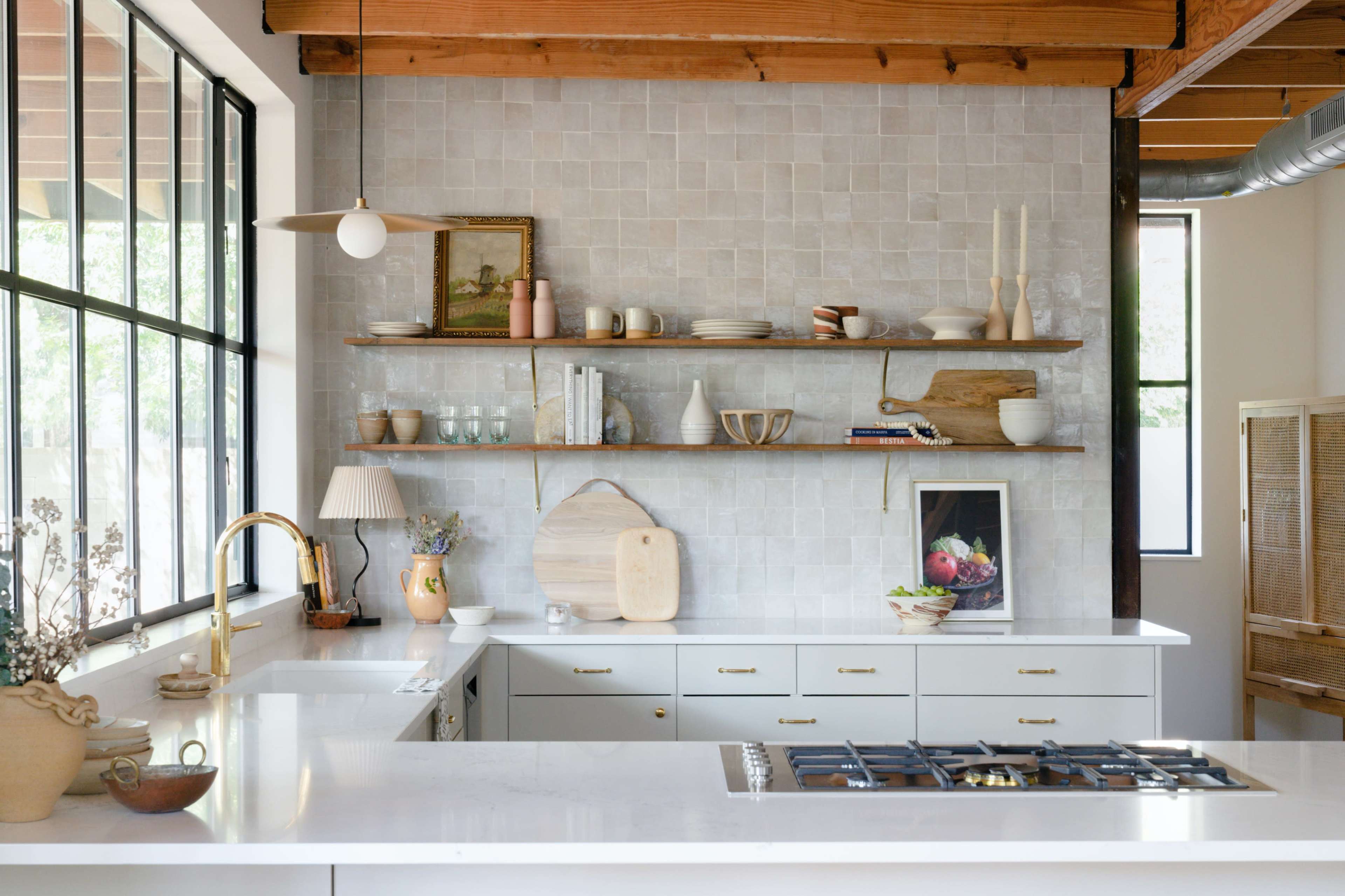 A modern kitchen with a white countertop, a gas stove, and open wooden shelves displaying various dishes and decor against a tiled wall.