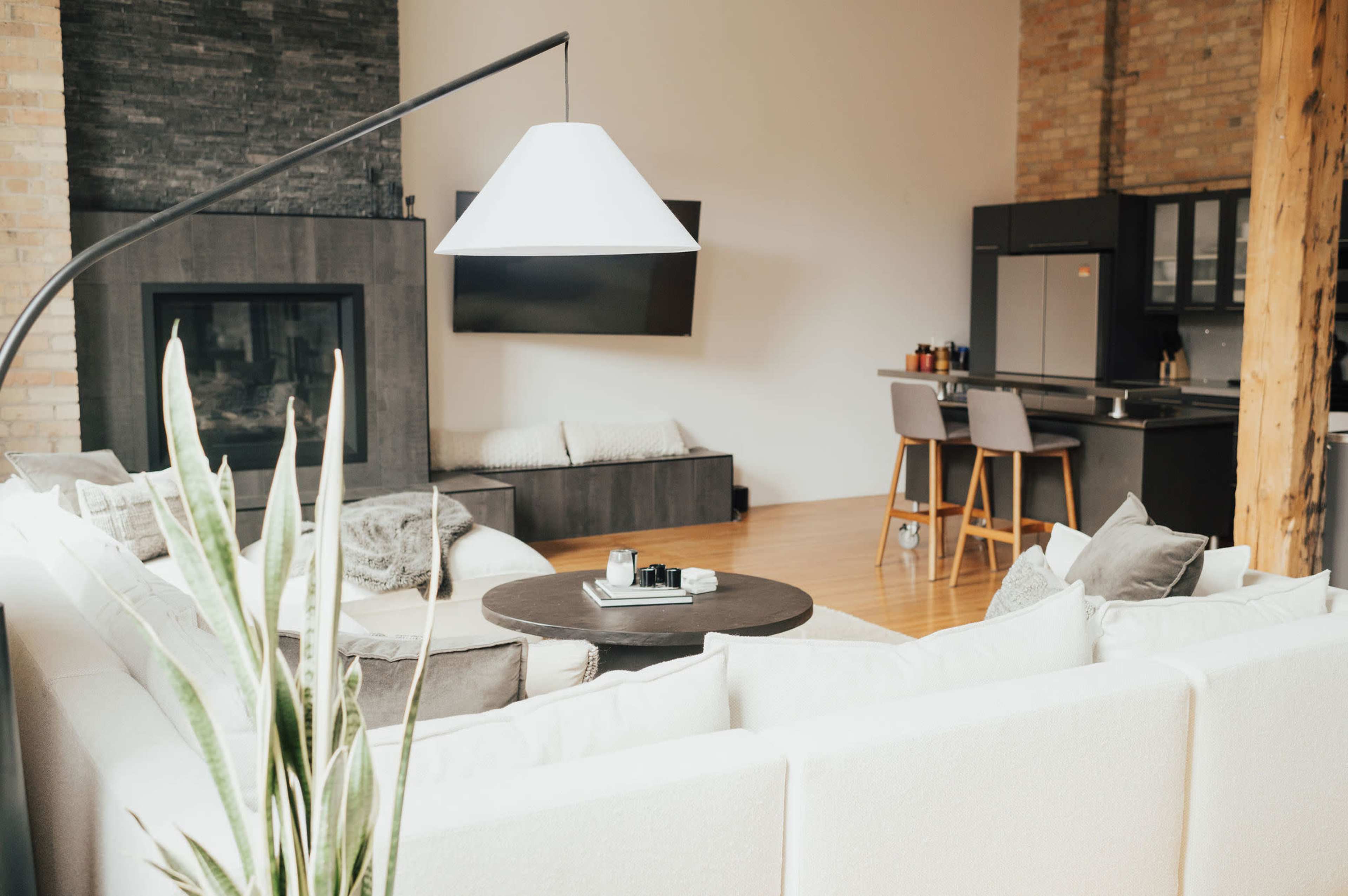 A spacious, modern living room with a large sectional sofa, a round coffee table, and a kitchen area visible in the background.