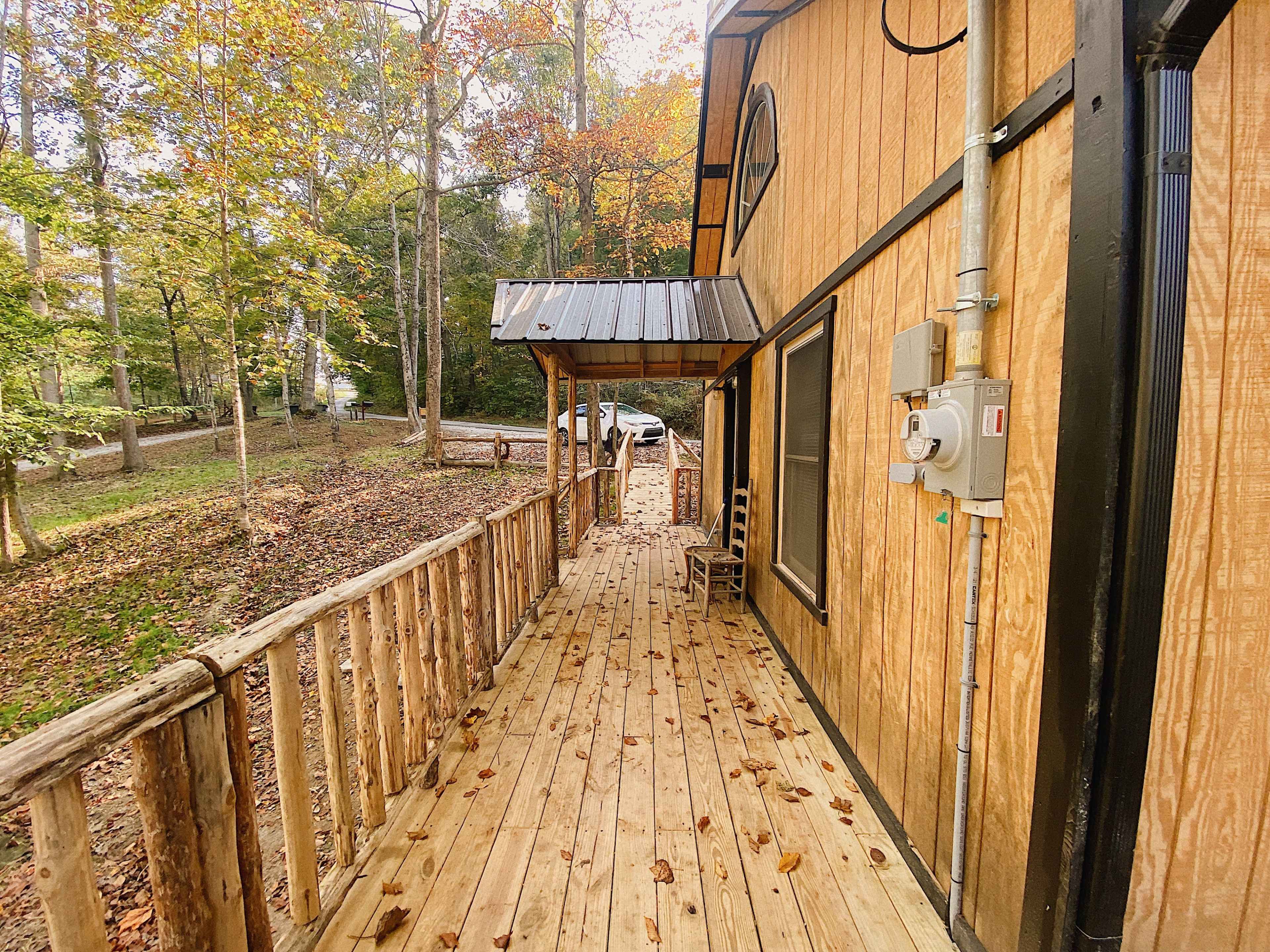 The image shows a wooden walkway leading to a house, with trees and fallen leaves in the surrounding area.