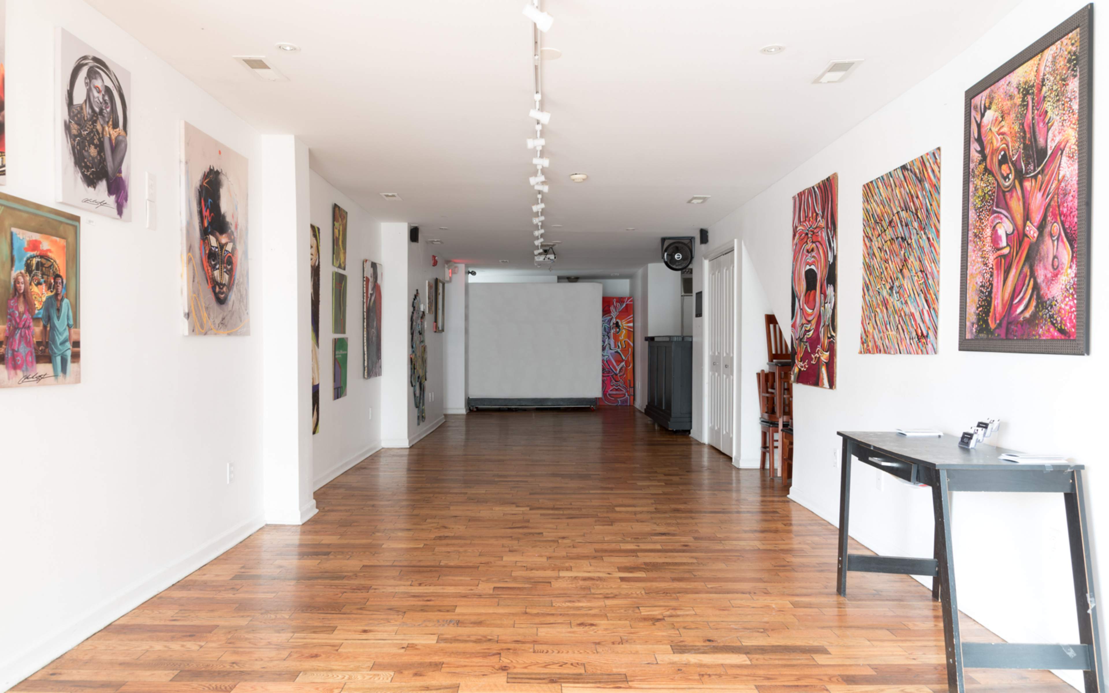 A spacious art gallery hallway with wooden floors and colorful artwork displayed on the white walls.