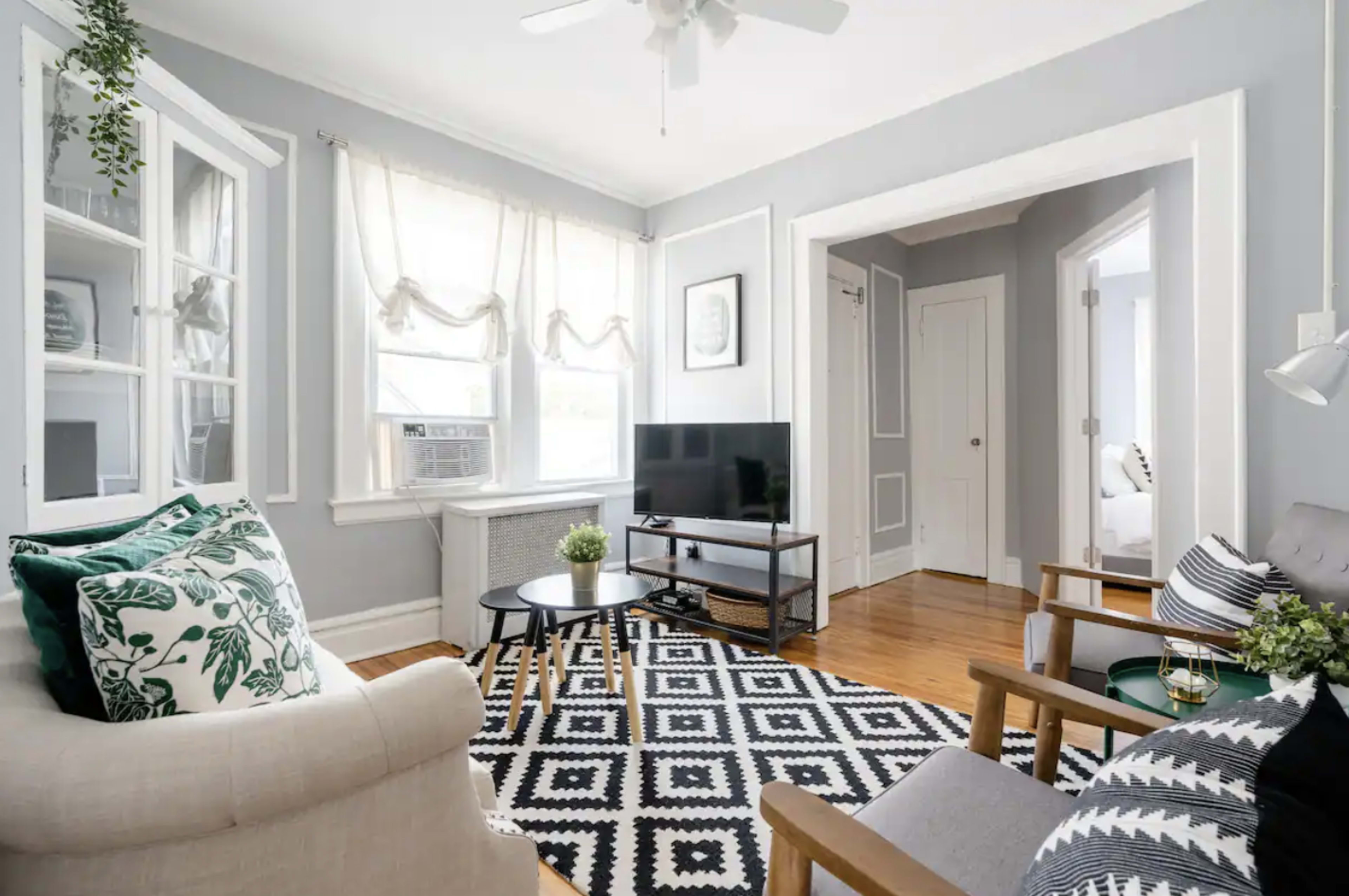The image shows a modern living room with a television, a patterned rug, and an arrangement of furniture including a sofa and a coffee table.