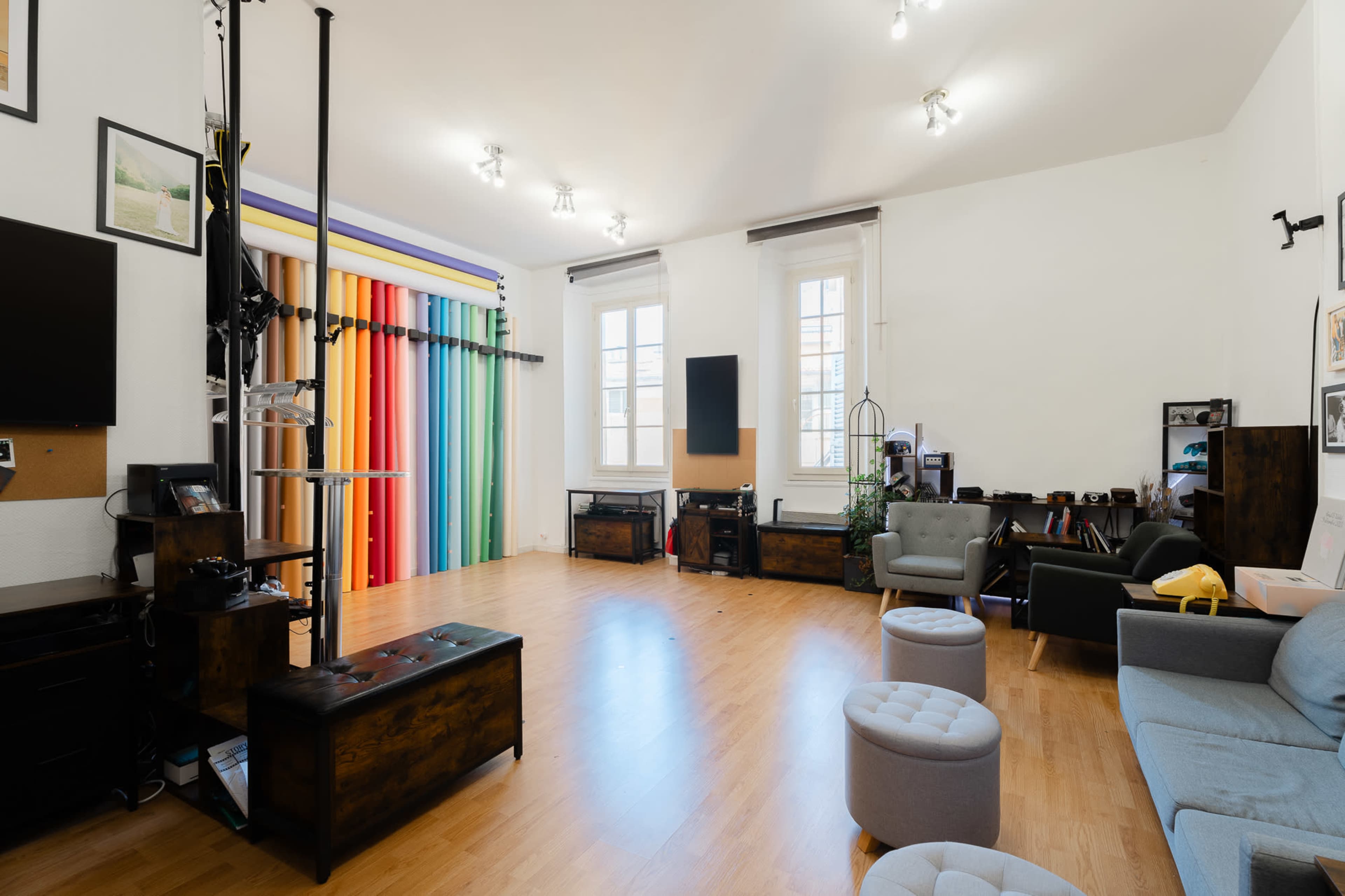 The image shows a brightly lit studio space with colorful backdrops, seating areas, and various photography equipment along the walls.