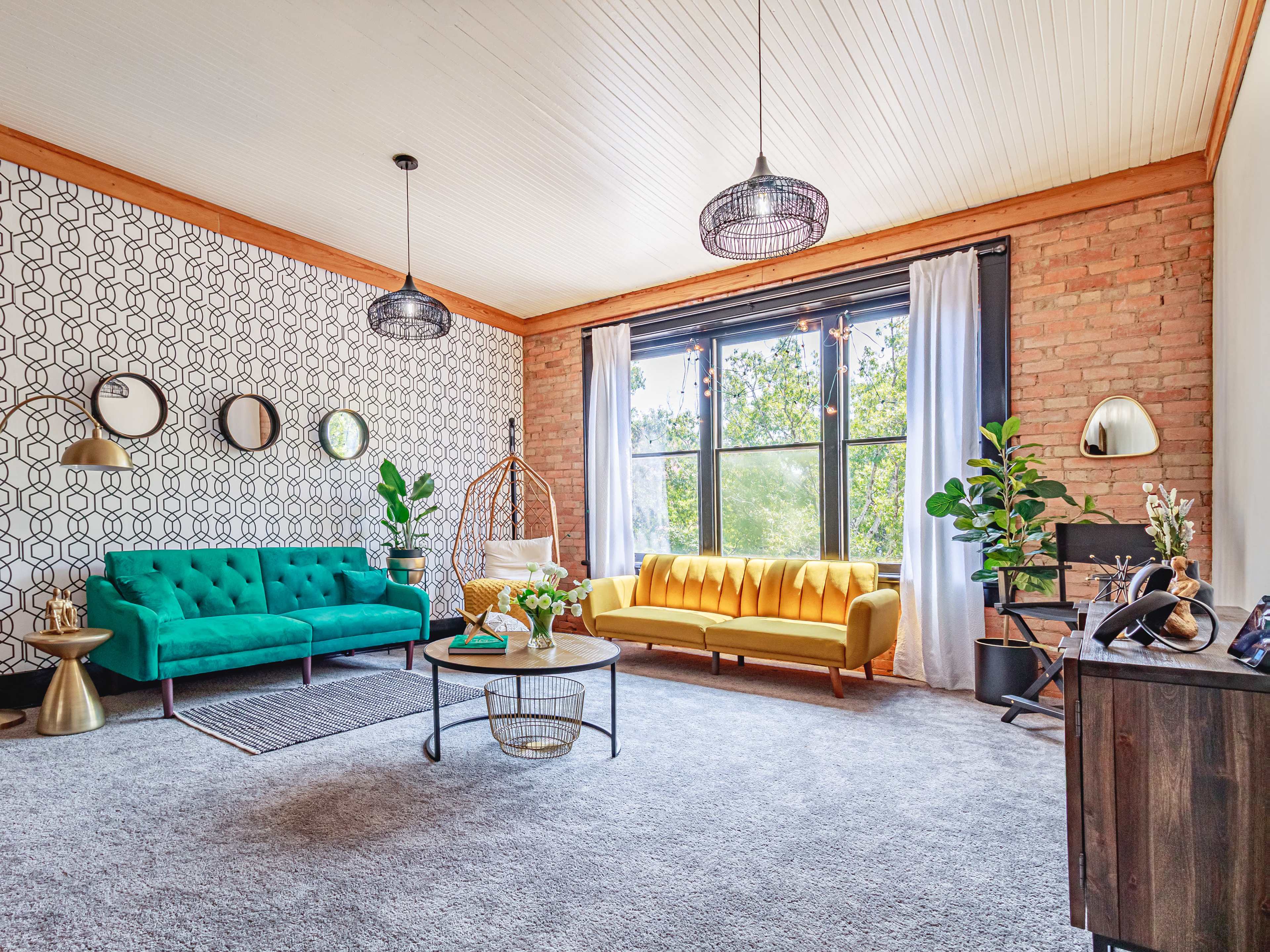 The image shows a modern living room with a green tufted sofa, a yellow sofa, a round coffee table, and large windows with natural light illuminating the space.