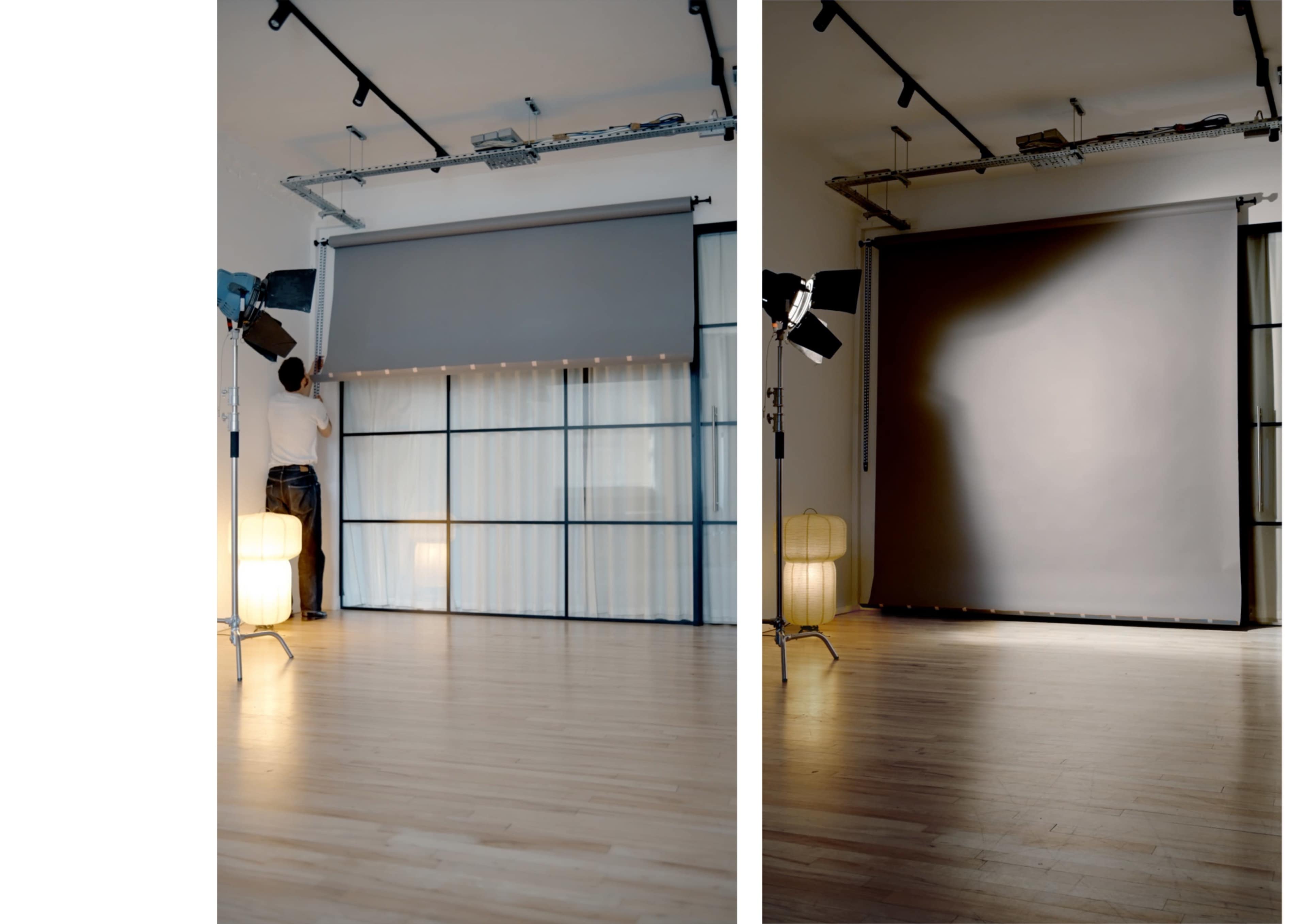 A person is adjusting a large curtain in a spacious, well-lit room equipped with studio lighting and hardwood flooring.