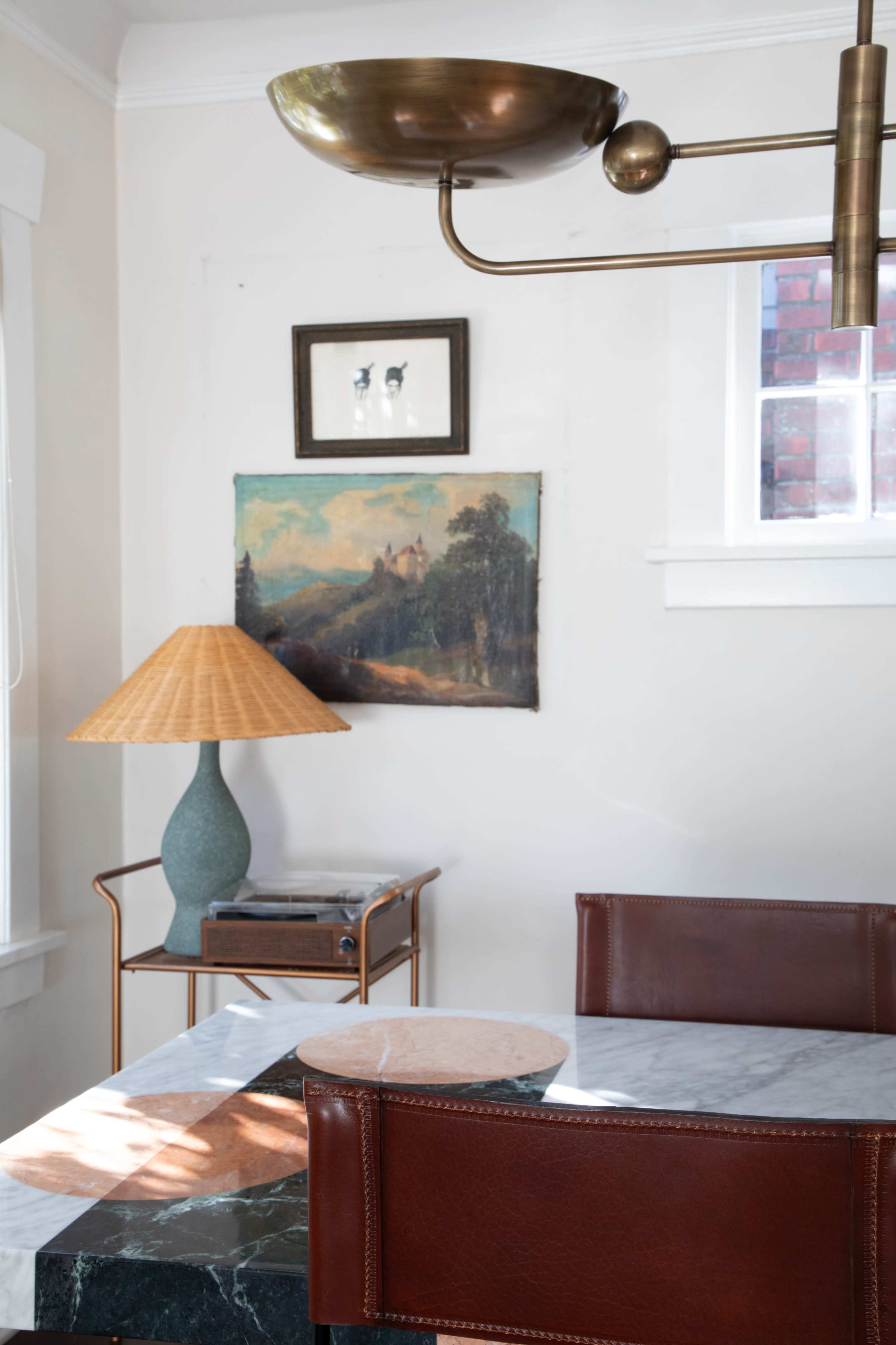 A table with a marble top is positioned near a lamp and a painting on the wall in a well-lit room.