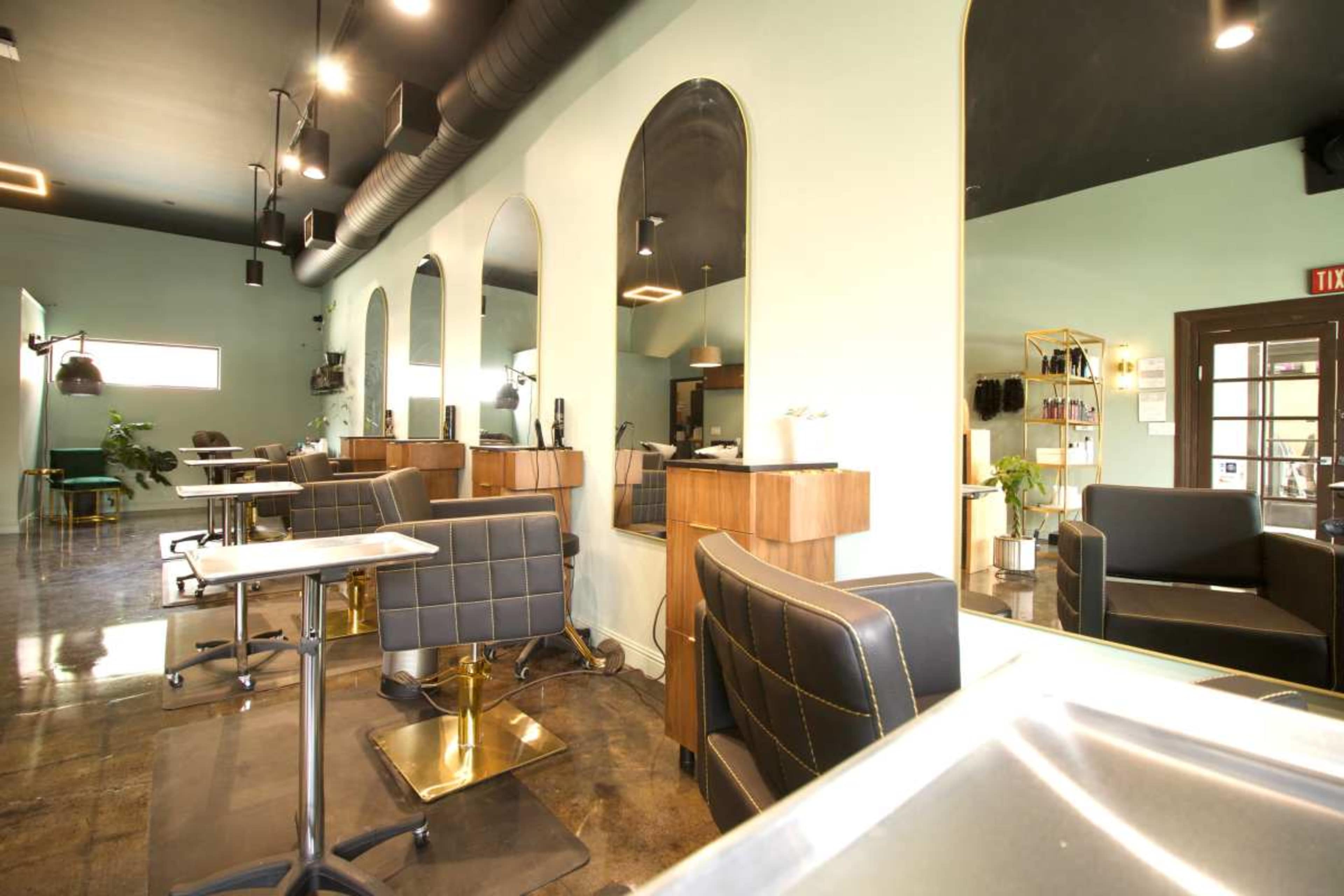 The image shows a modern hair salon interior with stylist stations, seating areas, and green walls.