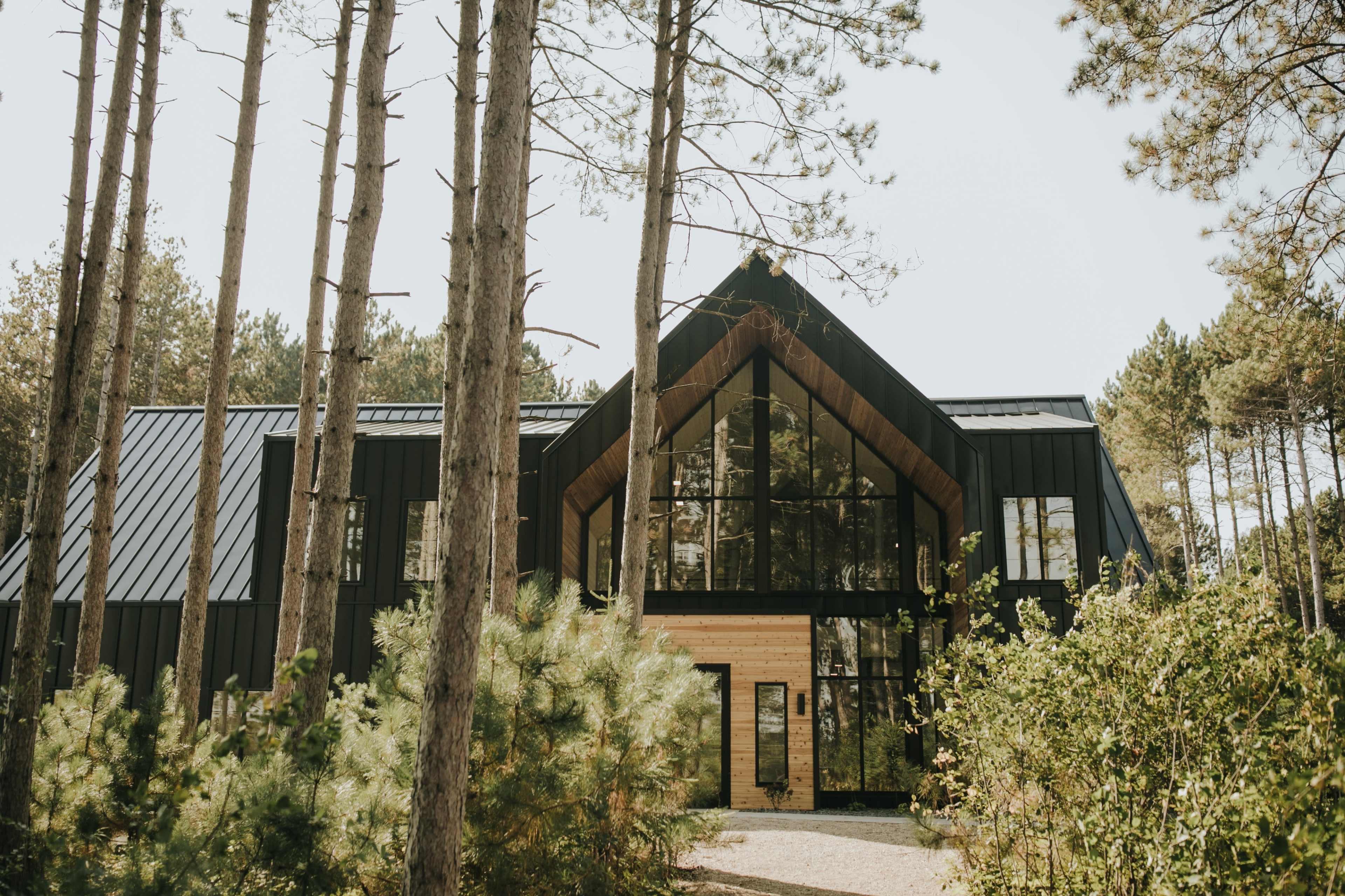 A modern black timber house with large glass windows is surrounded by tall trees and greenery.