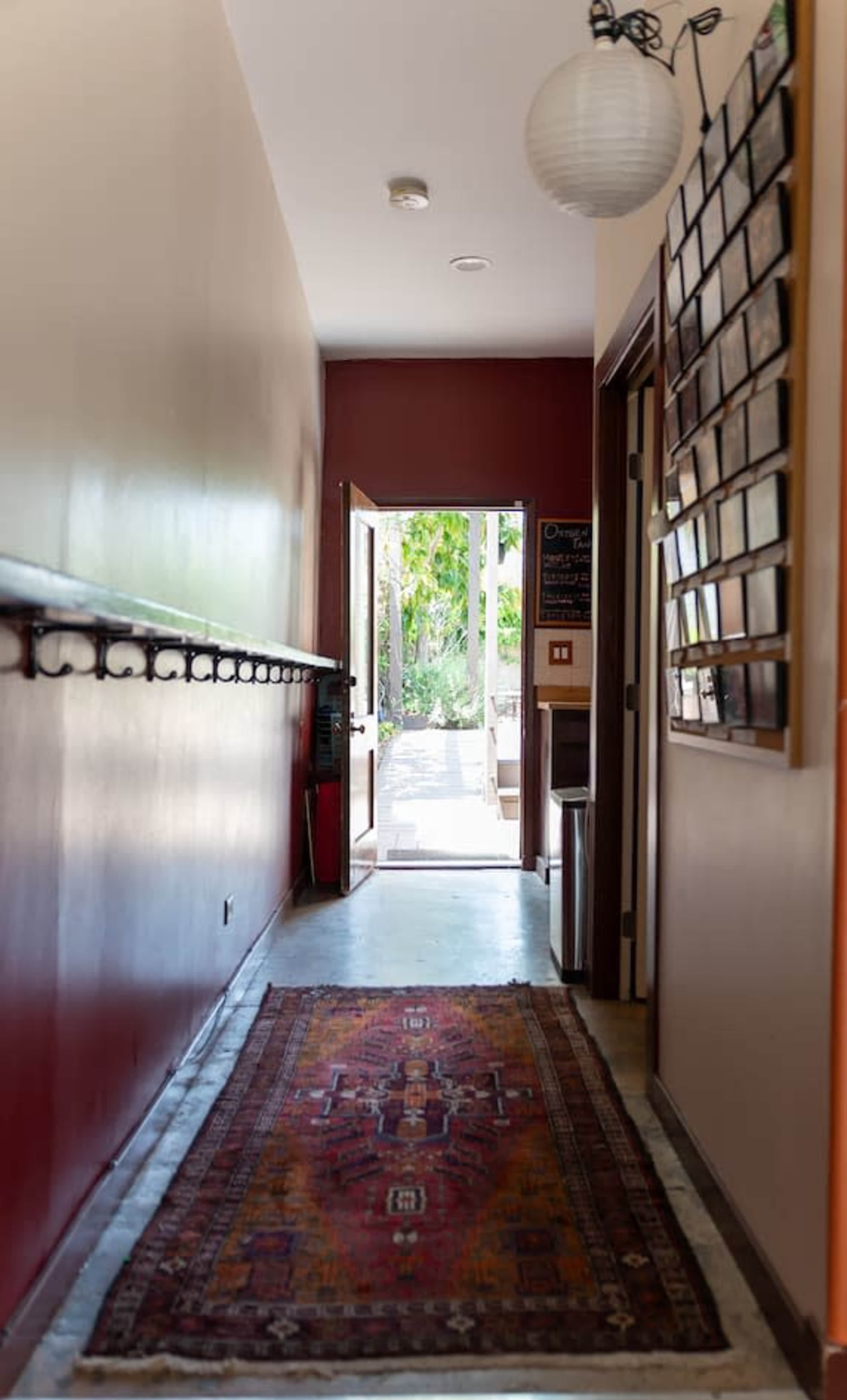 A narrow hallway with a patterned rug leads to an open door at the far end, revealing a view of a garden outside.