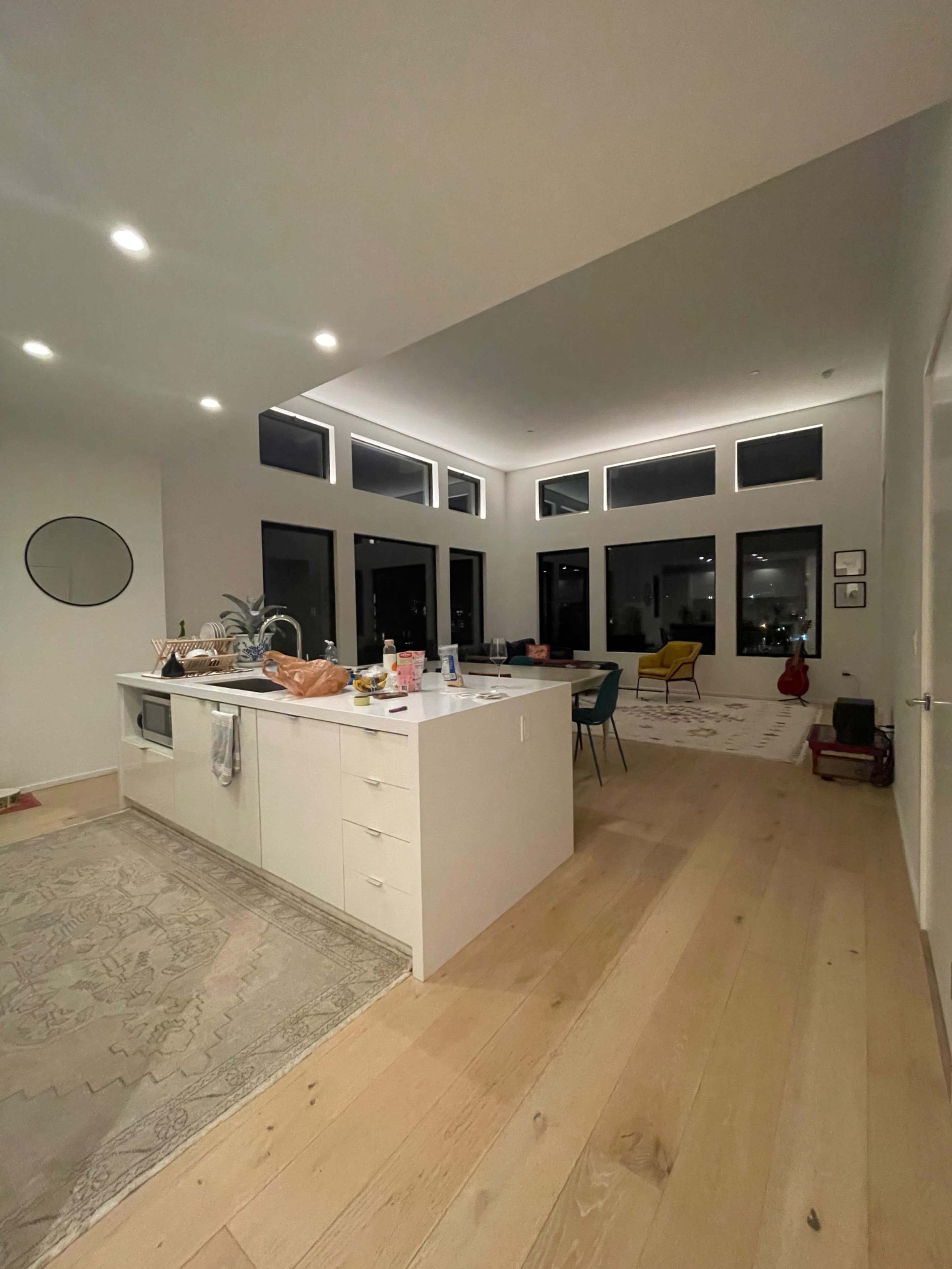 A modern kitchen with a large island and a spacious living area filled with natural light from multiple large windows.