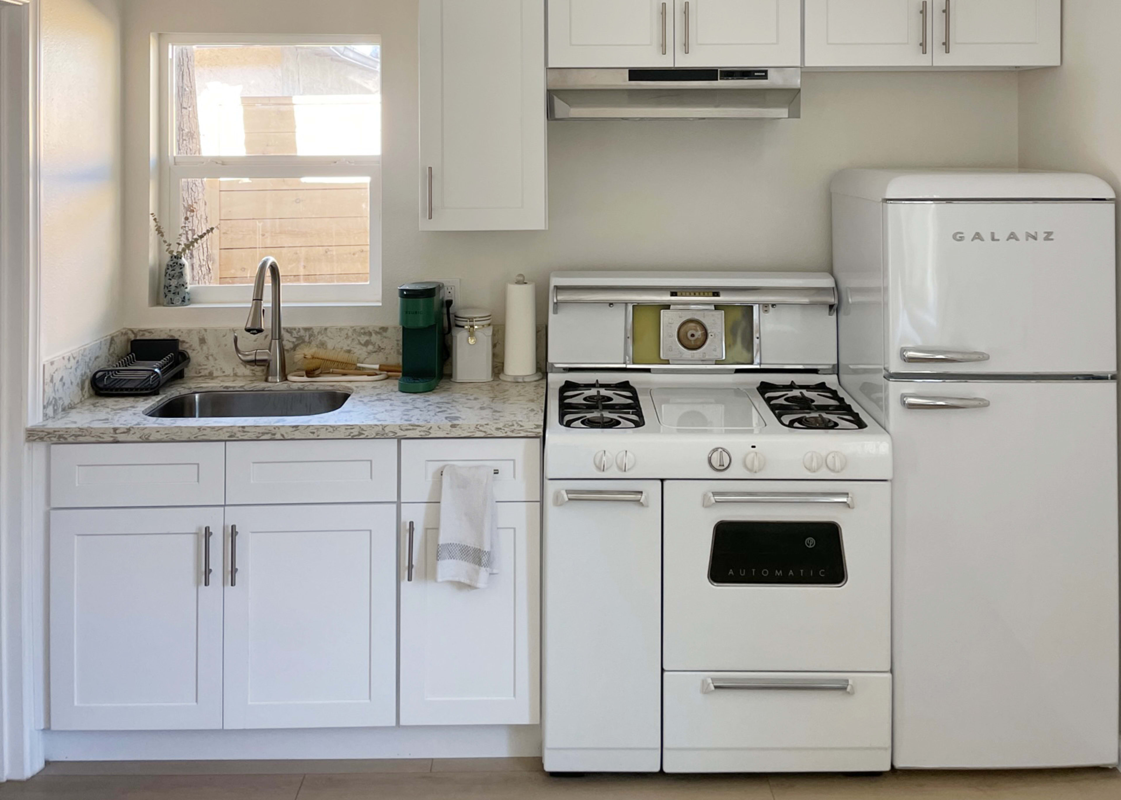A modern kitchen with white cabinetry, a stainless steel sink, a gas stove, and a retro-style refrigerator.