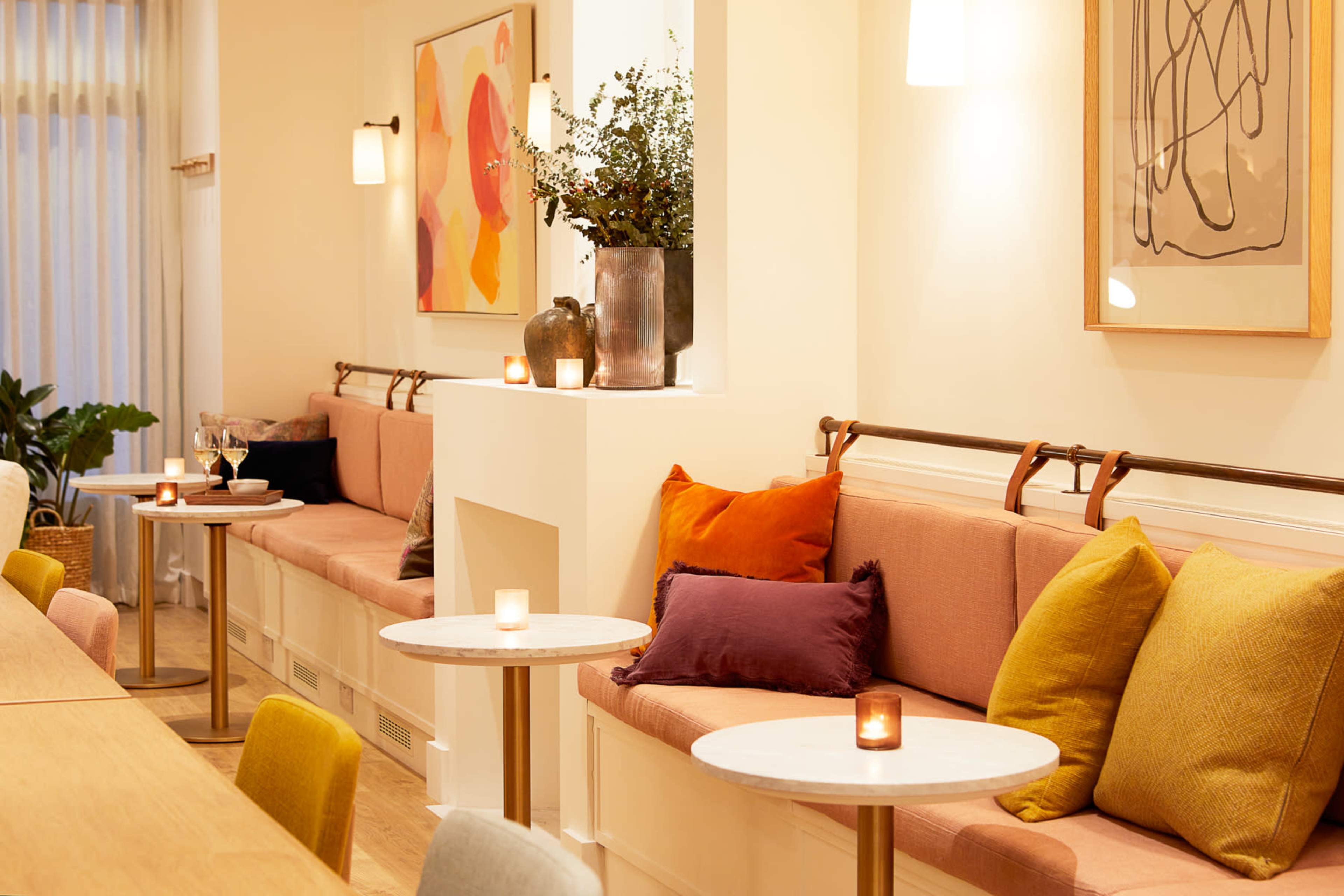 A cozy cafe interior with soft seating, small round tables, and decorative art on the walls.