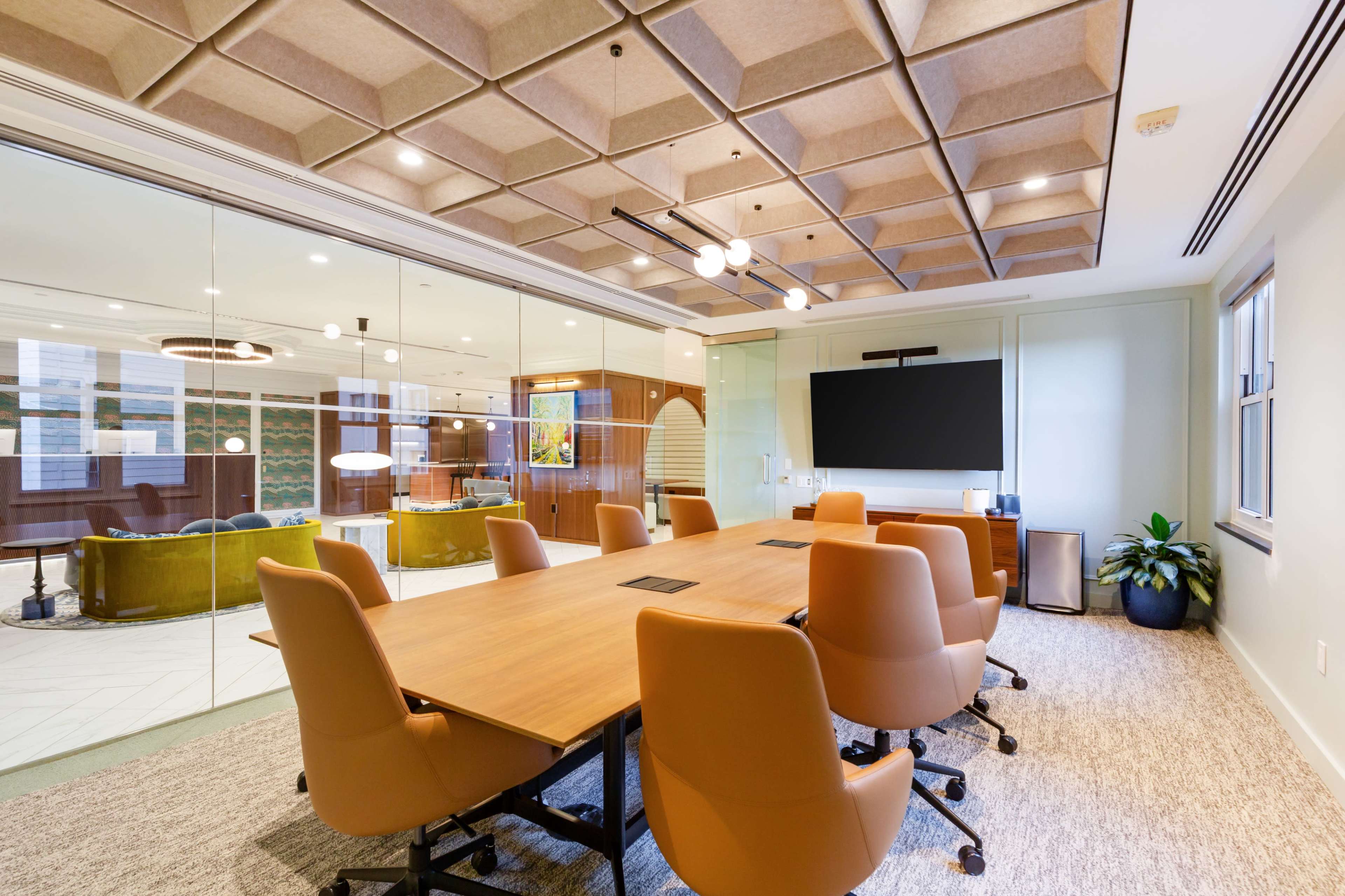 A modern conference room features a large wooden table surrounded by ergonomic chairs, with glass walls and a wall-mounted screen.