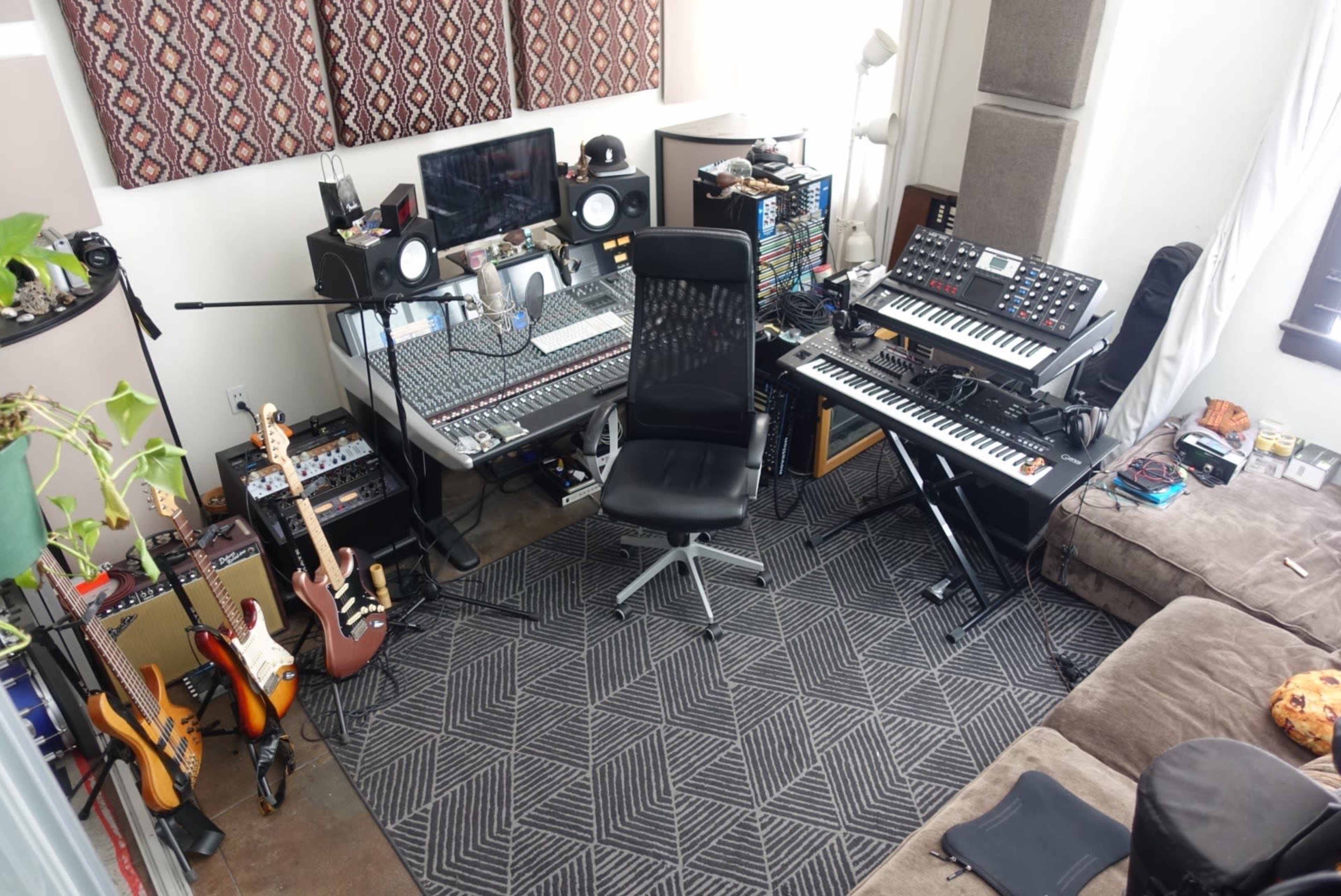 A music production room with a sound mixing console, keyboard, various musical instruments, and a workstation chair arranged around a cozy seating area.