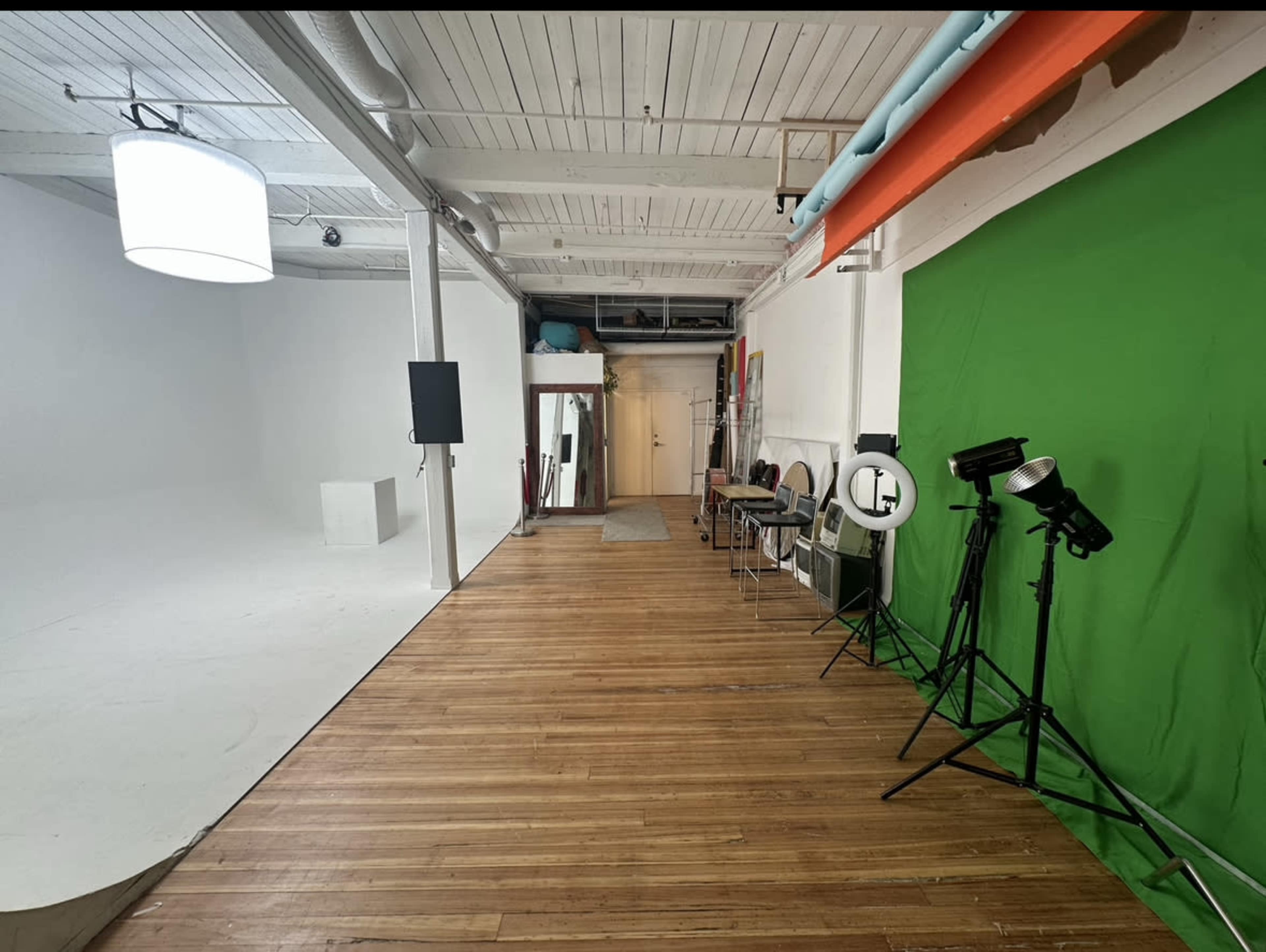 The image shows a spacious studio with a green screen, wooden flooring, and various lighting equipment on one side.
