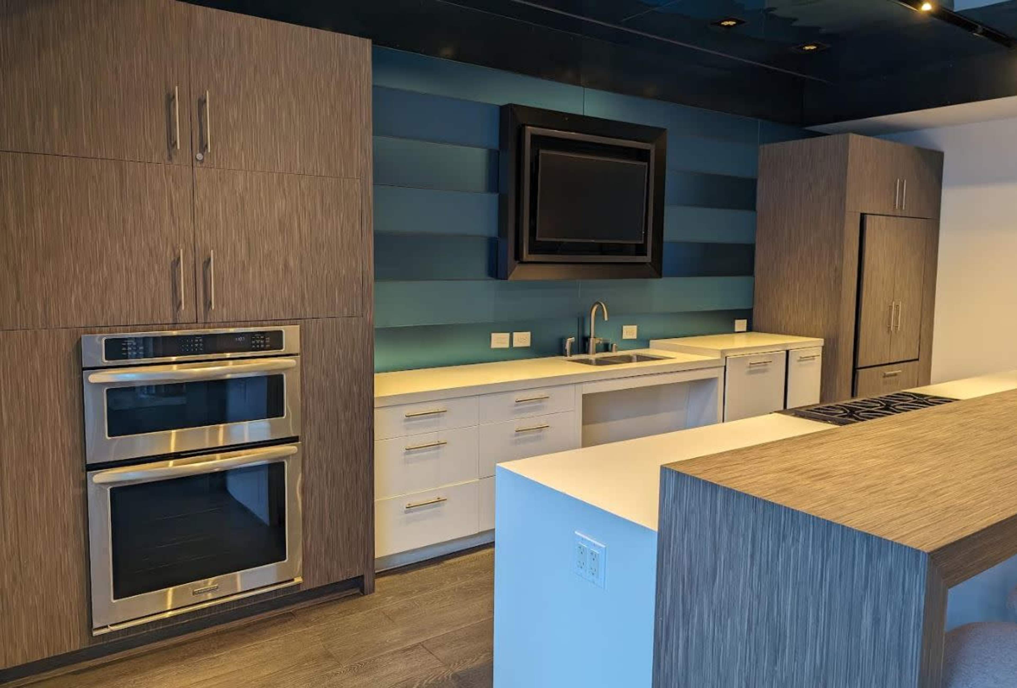 A modern kitchen with built-in appliances, a sink, and a large countertop, featuring a combination of textured wood and blue paneling on the walls.