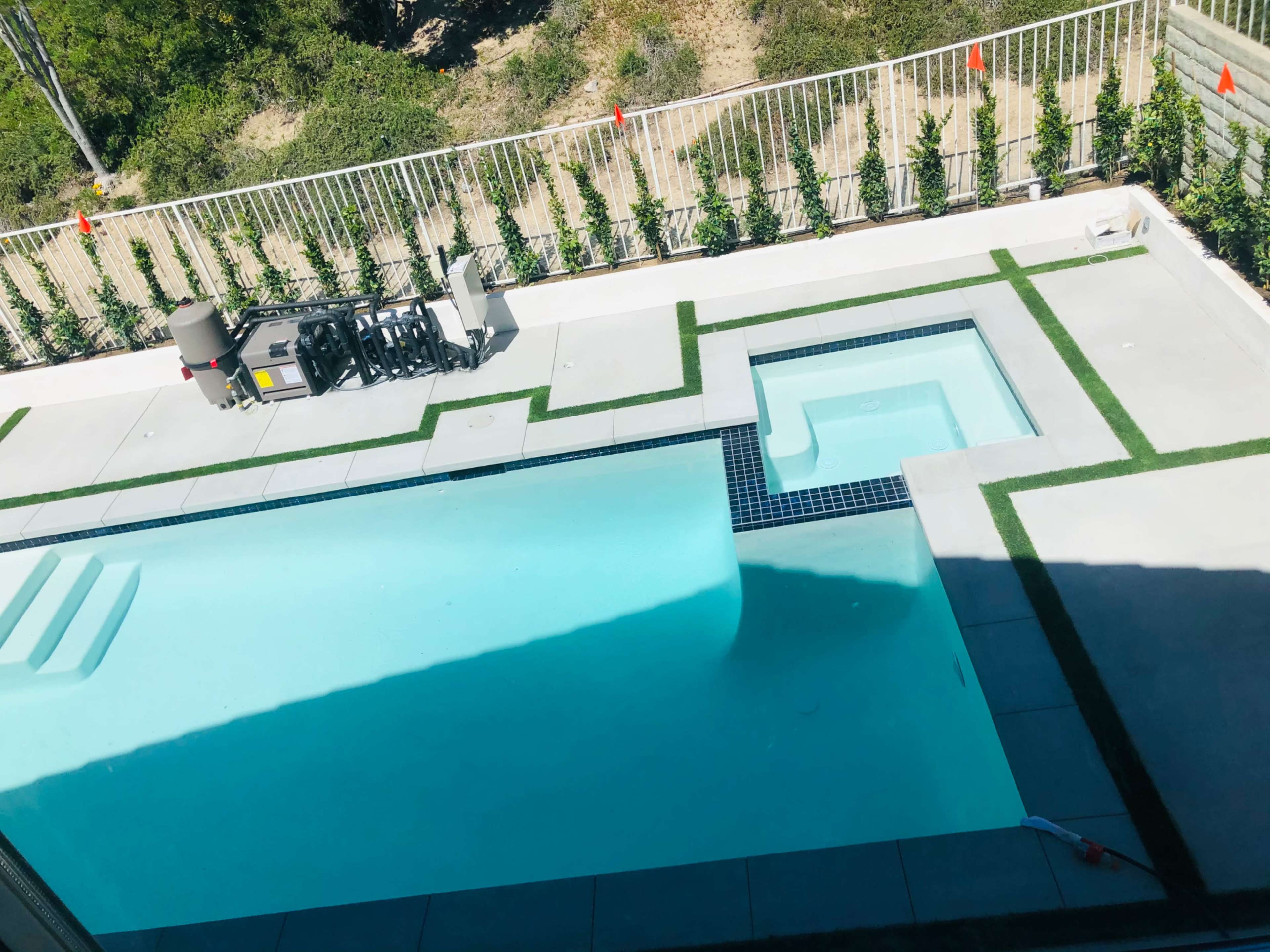 A modern swimming pool with a connected hot tub, surrounded by a concrete patio and a green lawn border.