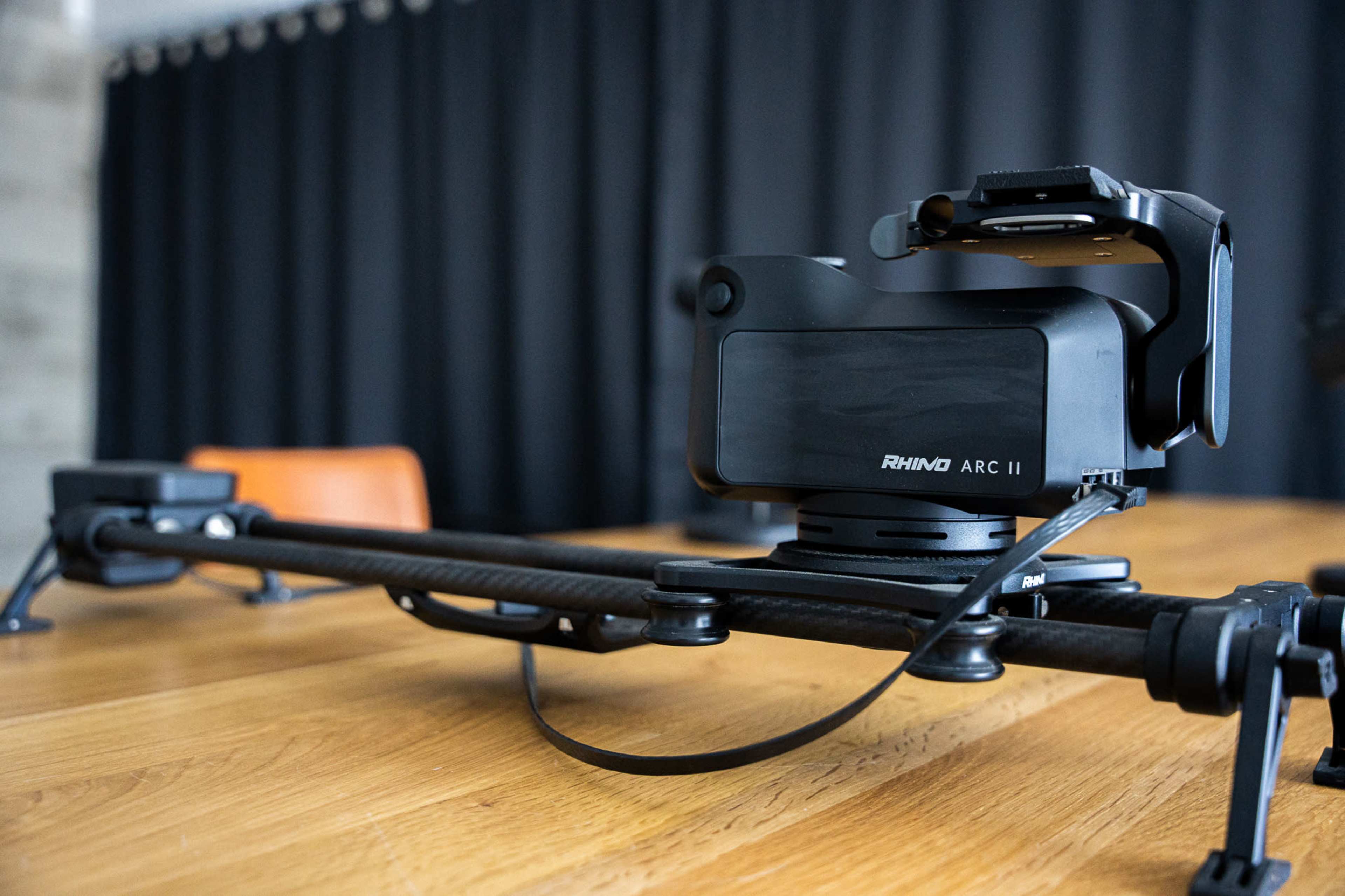 A camera slider is positioned on a wooden table with a camera mounted on it.