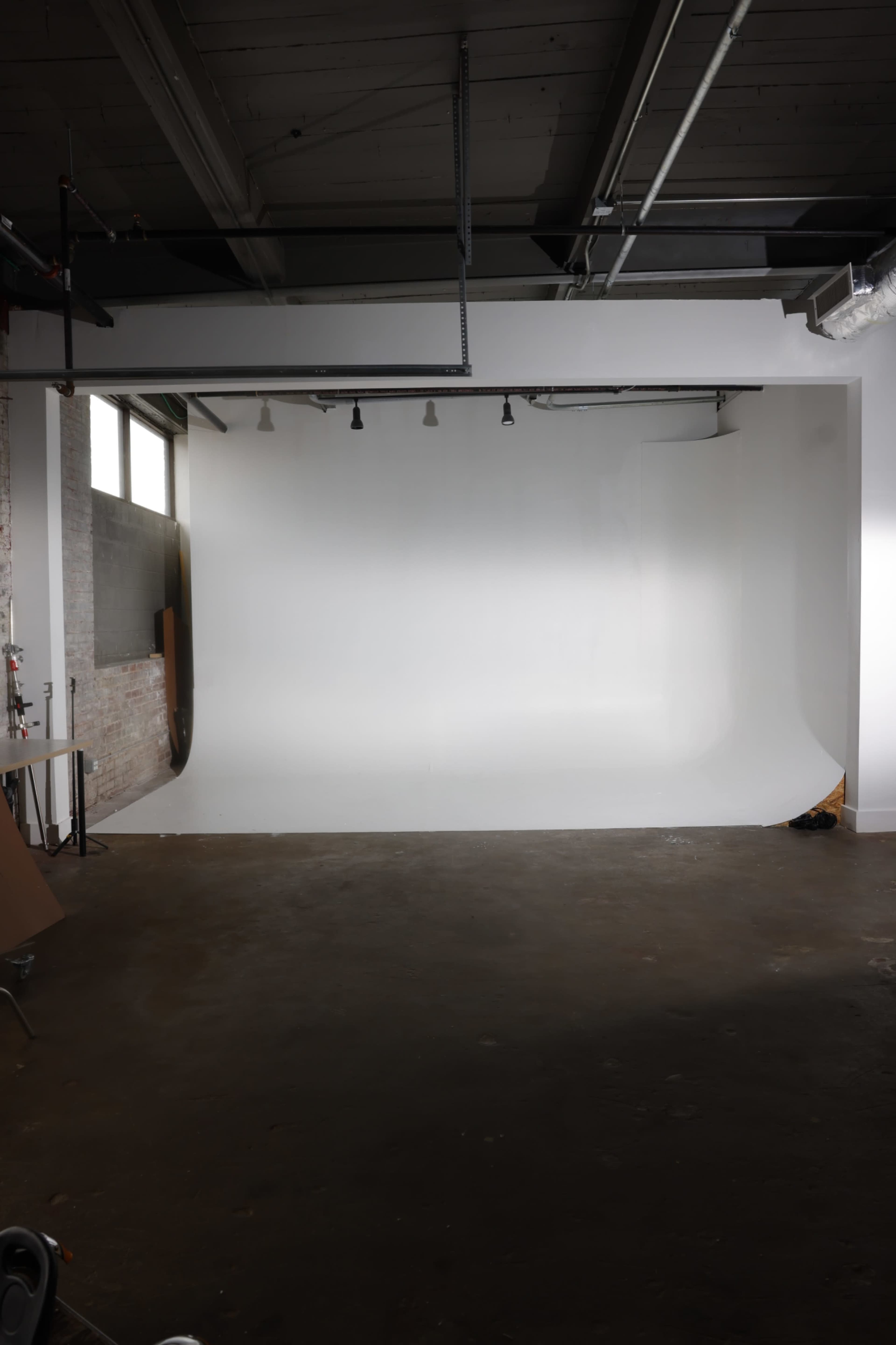 The image shows an empty photography studio with a seamless white backdrop and industrial-style lighting.