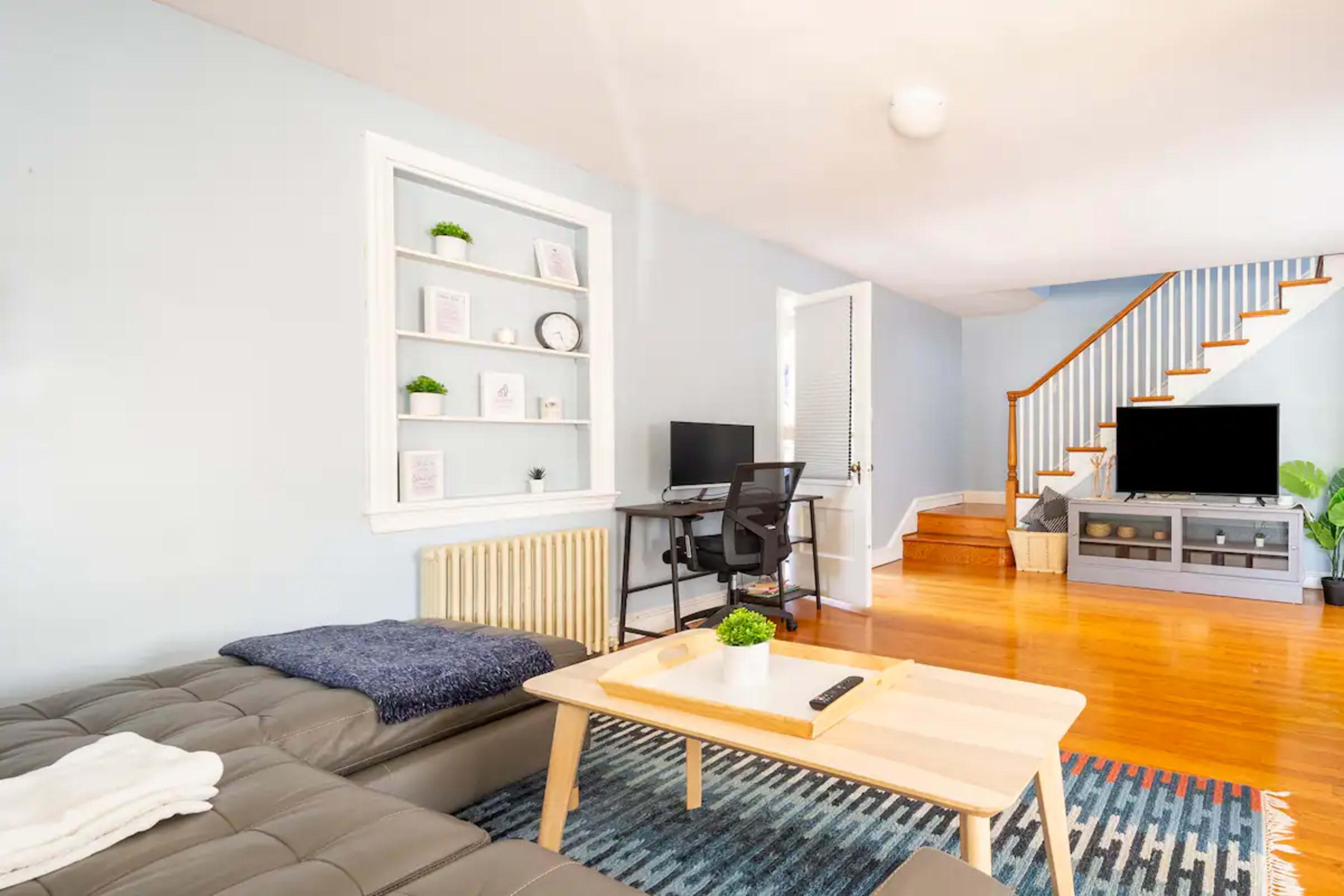 A light blue living room with a sectional sofa, a wooden coffee table, a computer desk, and a staircase leading to a different level.