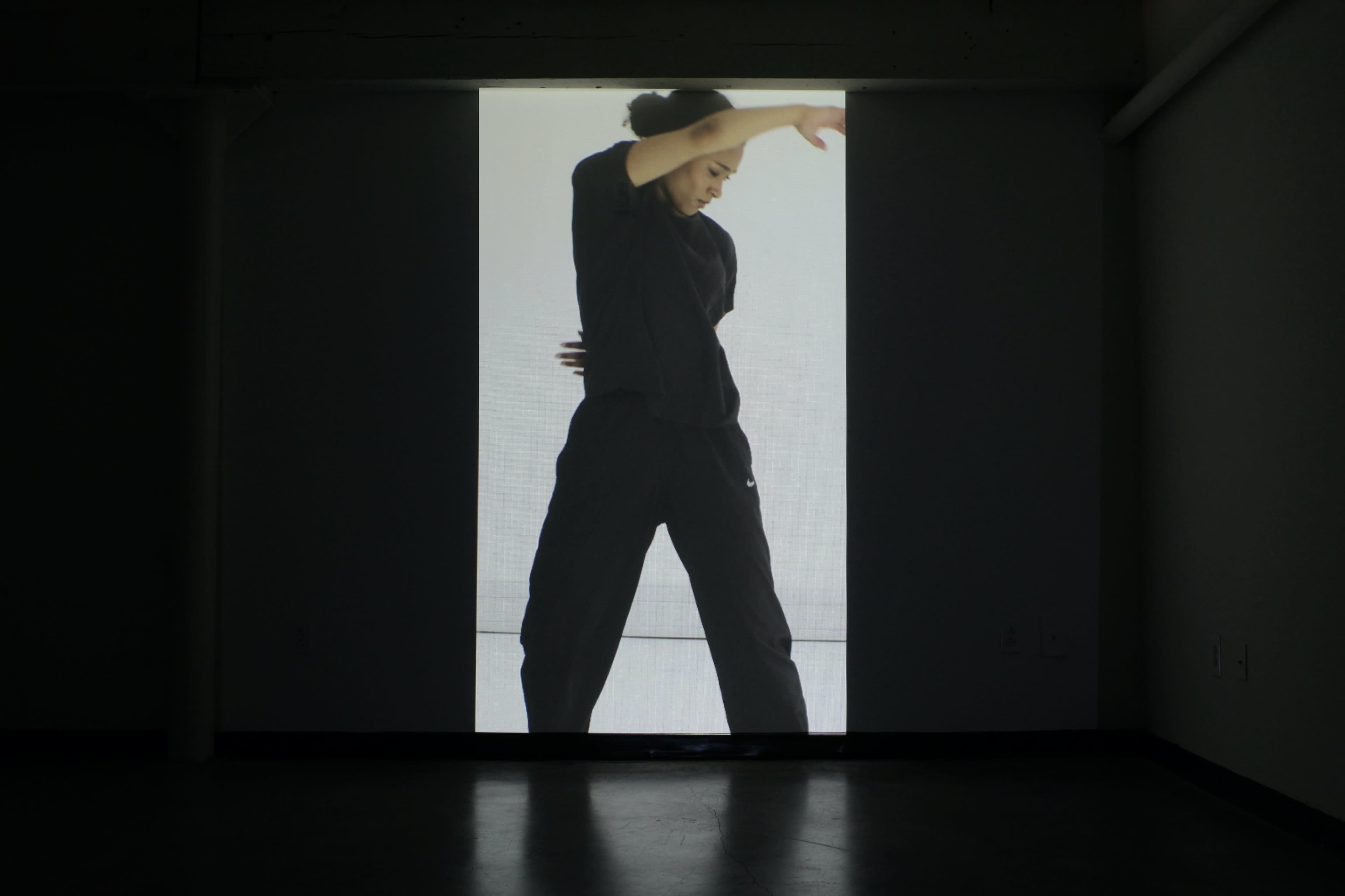 A dancer in a black outfit performs in front of a large, illuminated screen.