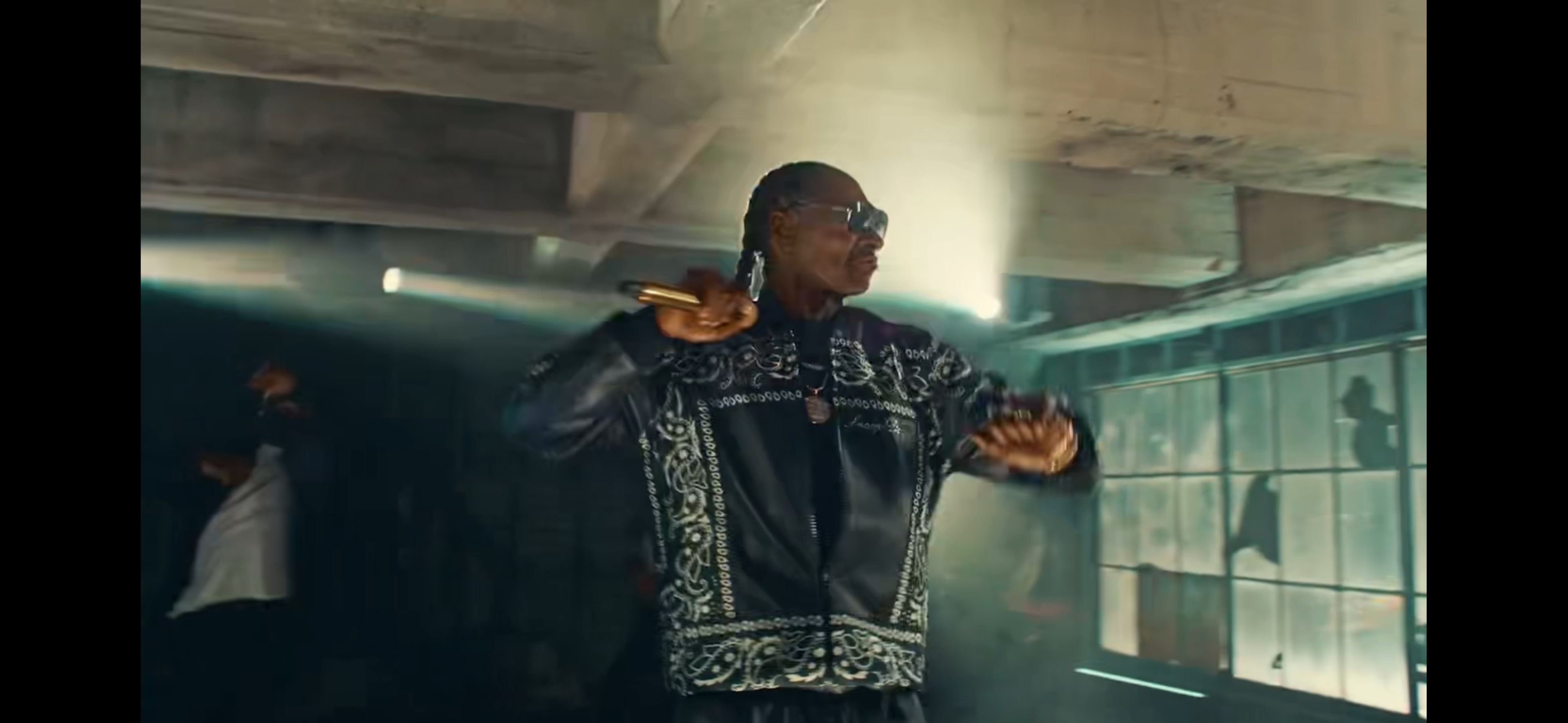 A man wearing a decorated black outfit performs on stage with dramatic lighting and shadows in the background.