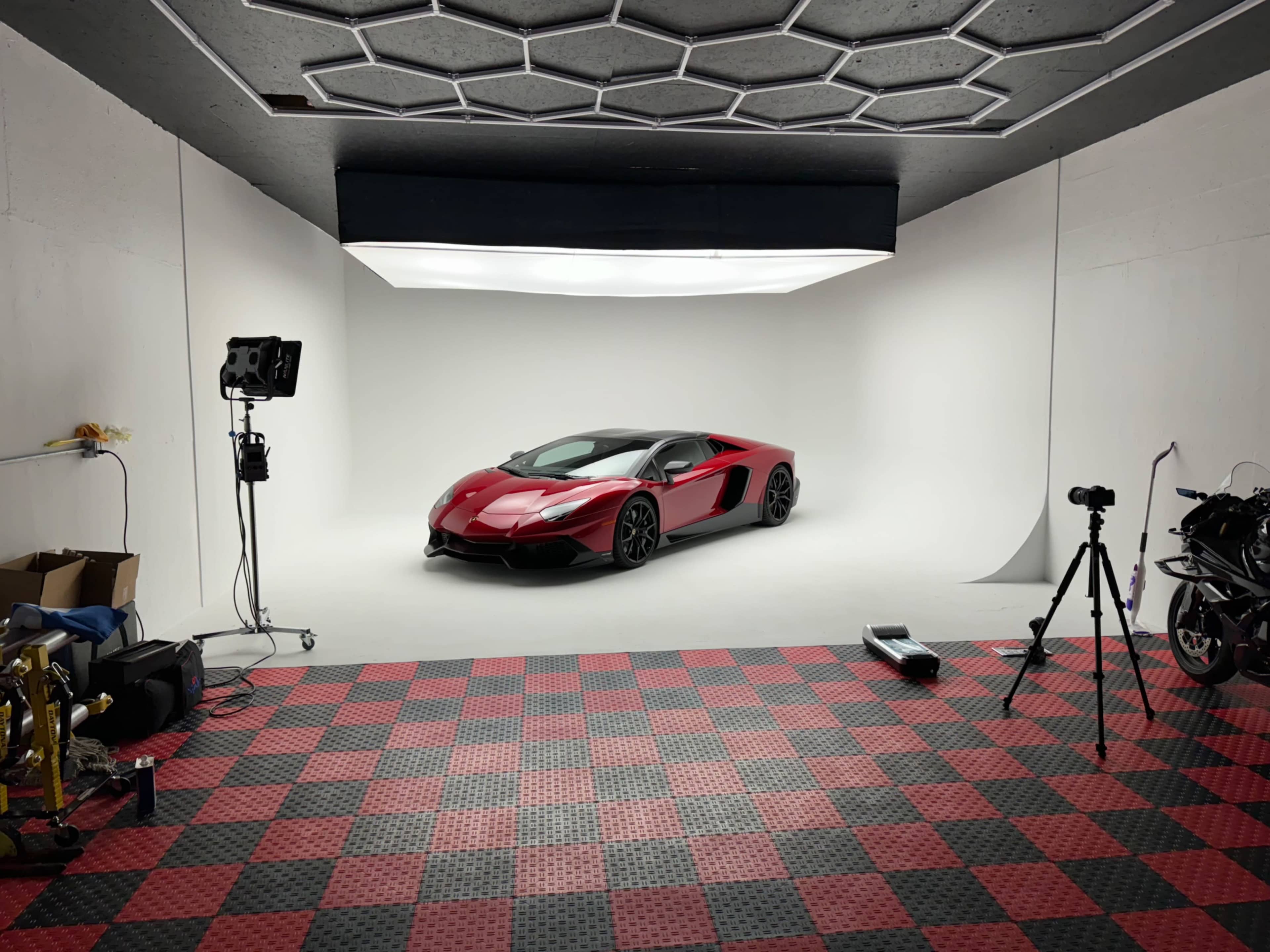 A red and black sports car is parked in a well-lit studio with a white backdrop and a checkerboard floor.