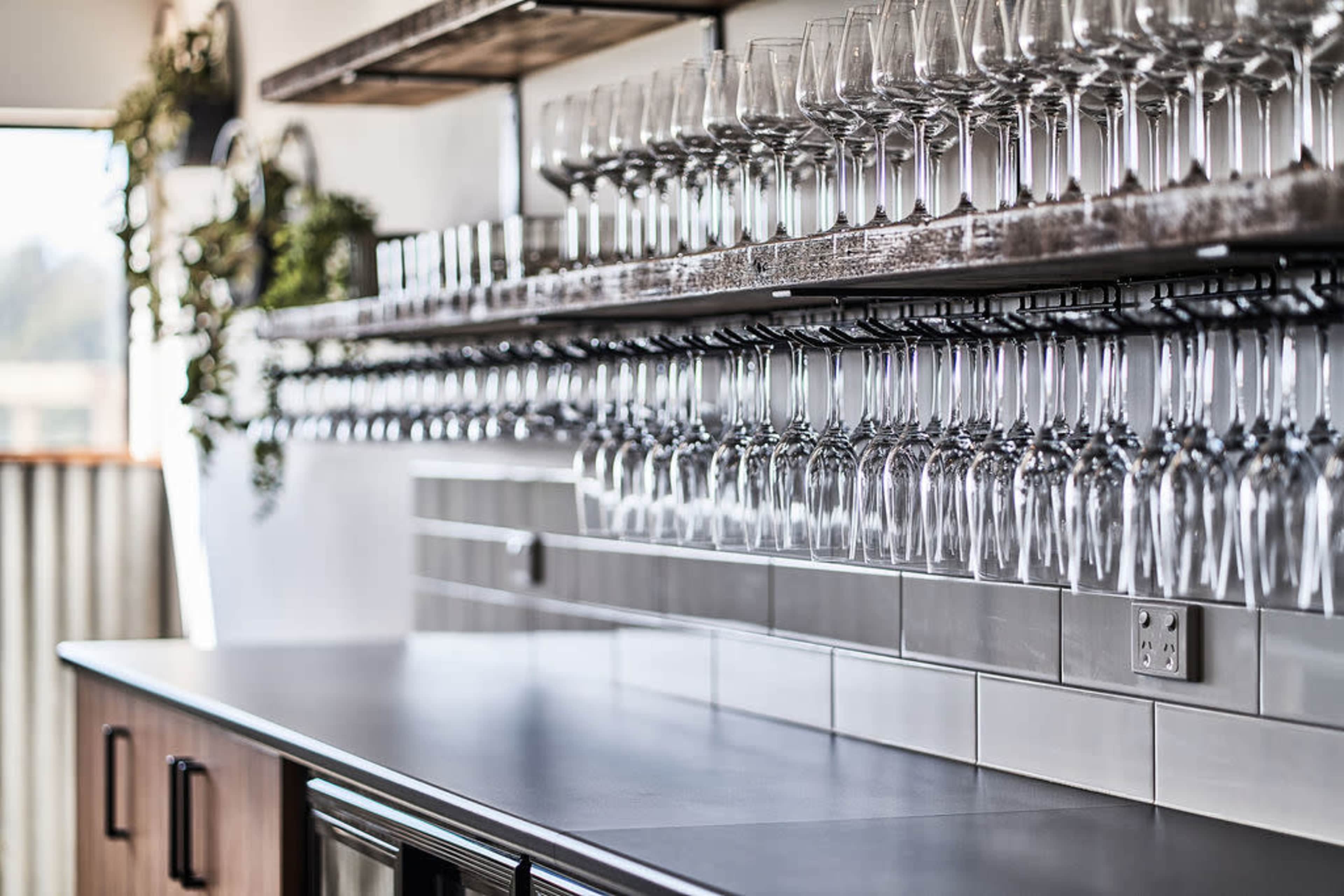 A neatly arranged row of wine glasses hanging upside down on a shelf above a counter in a modern kitchen or bar area.