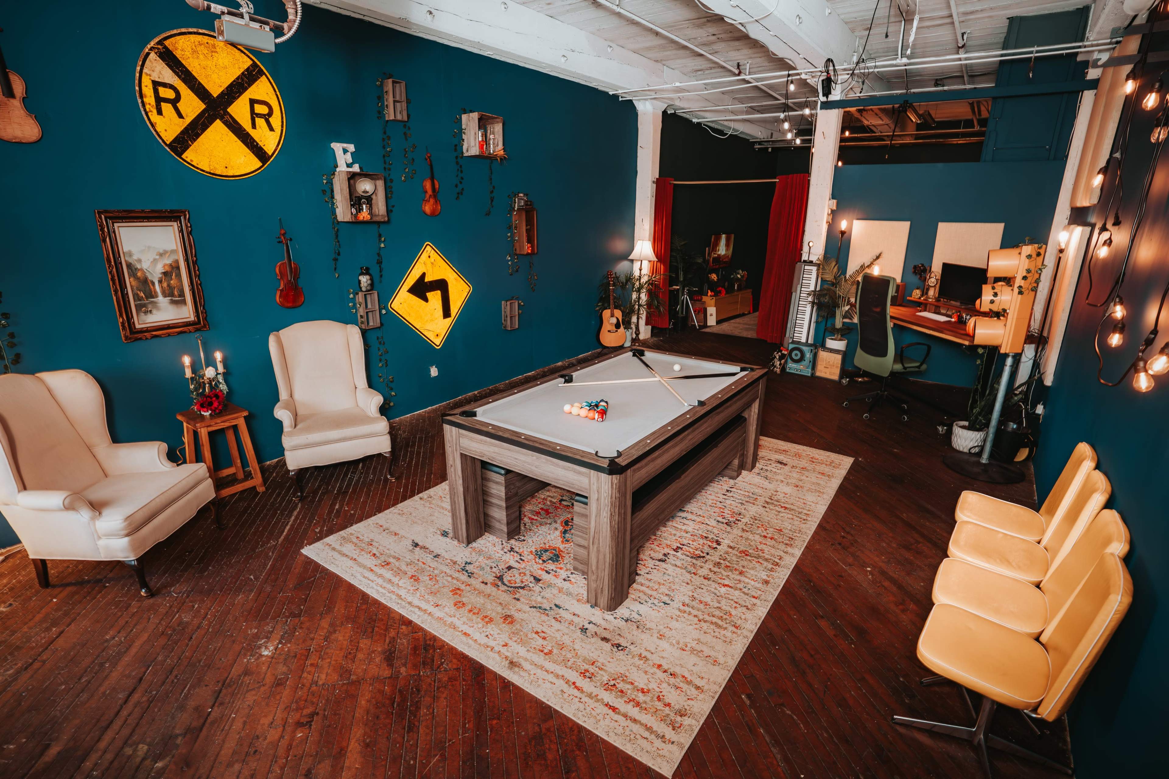 The room features a pool table at its center, surrounded by vintage furniture, musical instruments hanging on the walls, and various decorative signs.