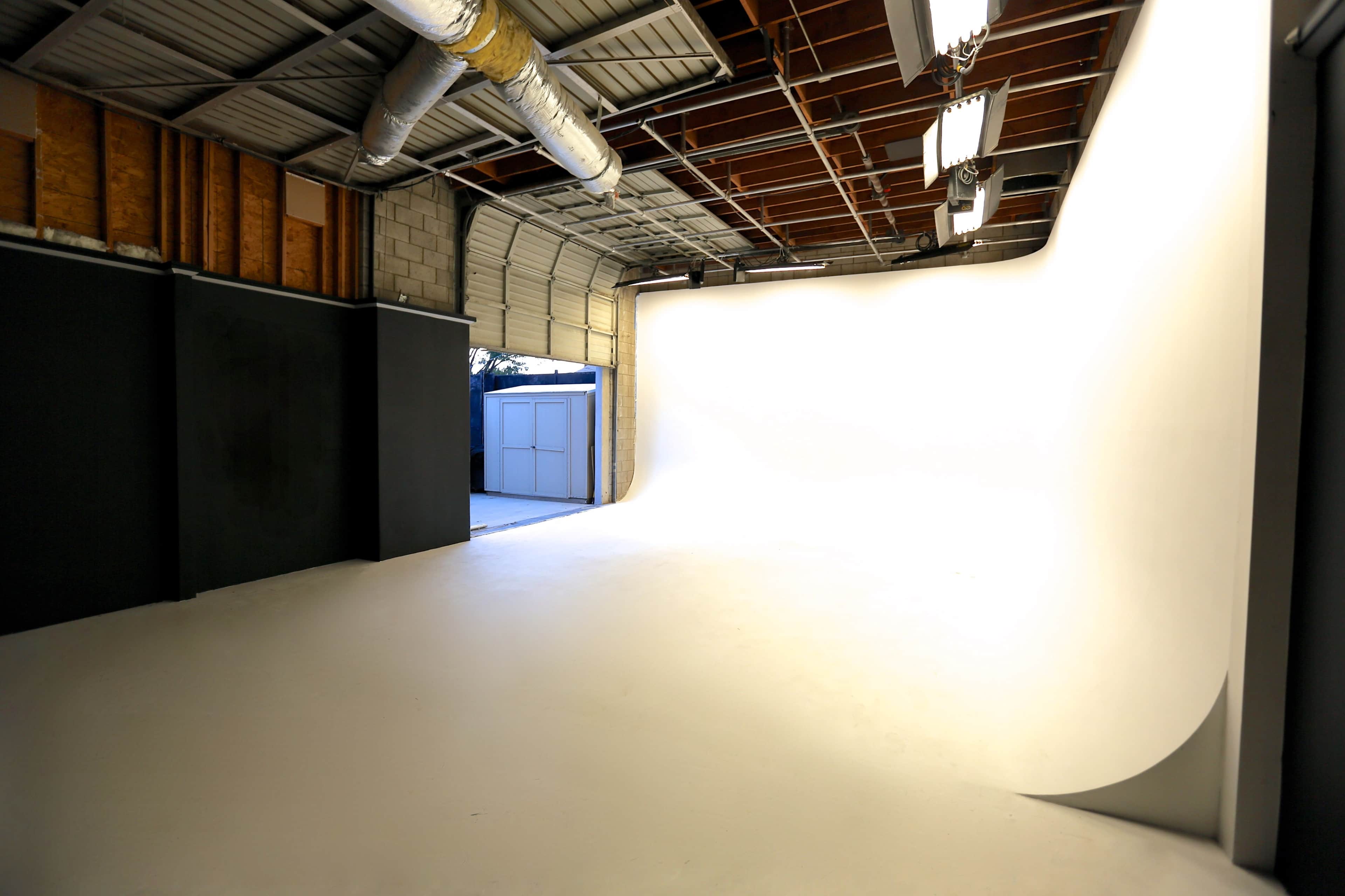 A spacious photography studio with a seamless white backdrop and an open door revealing an outdoor area.