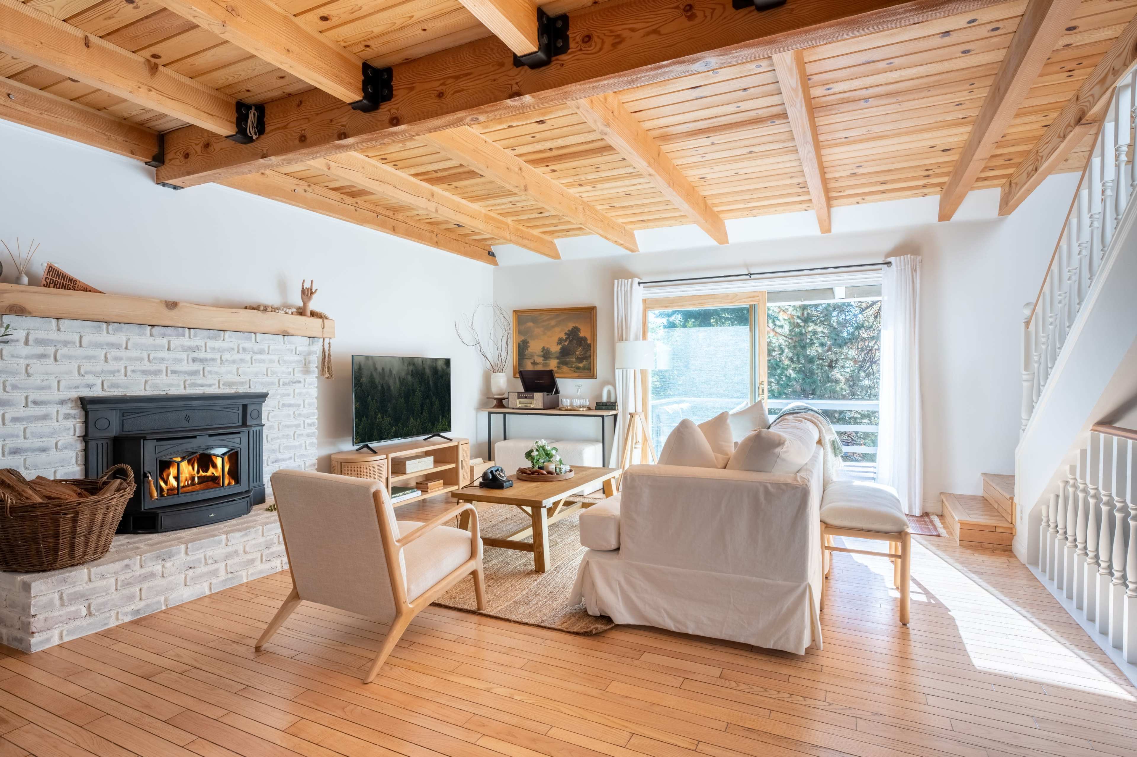A living room features wooden beams, a brick fireplace, contemporary furniture, and large windows allowing natural light.