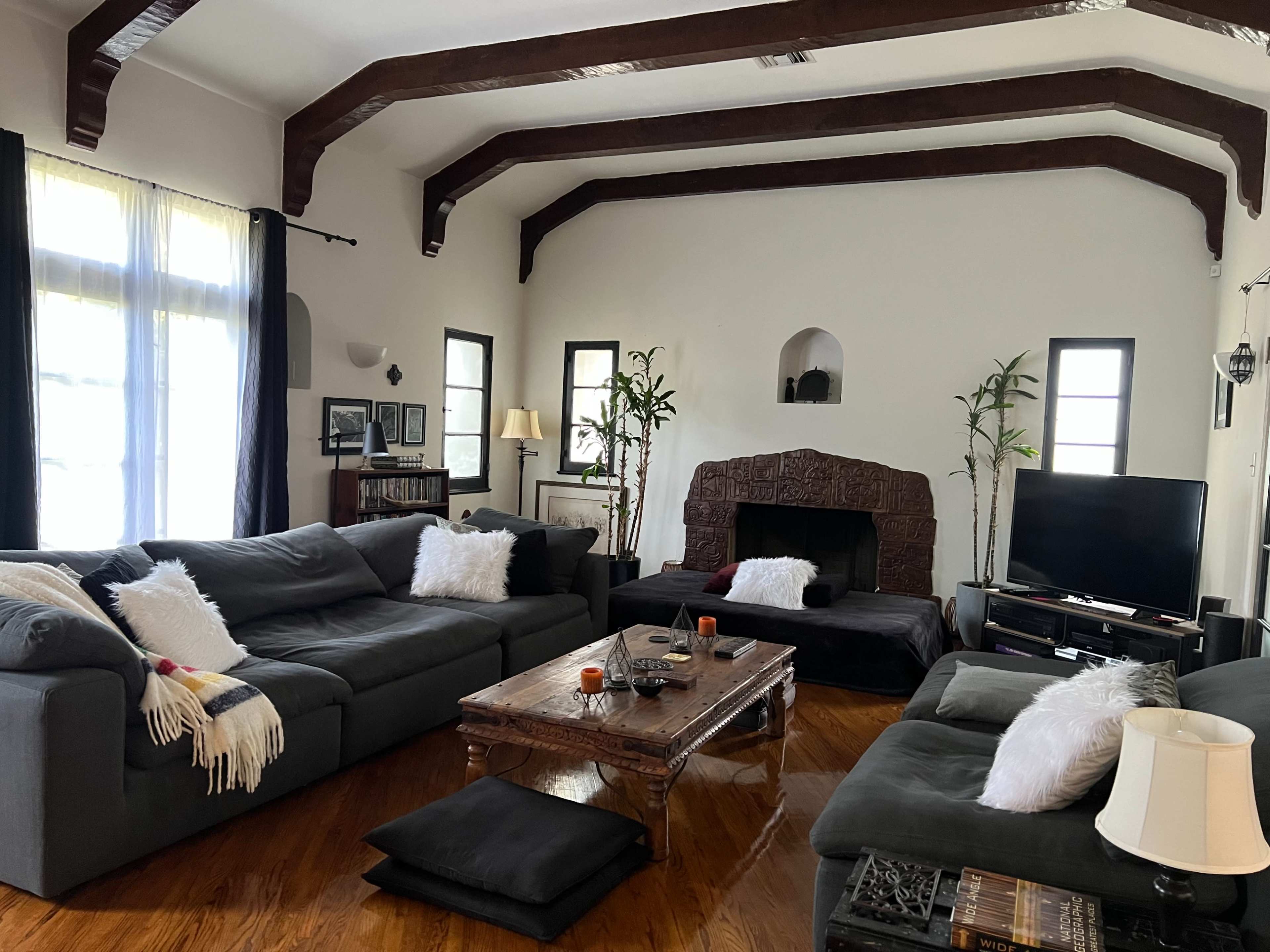 The living room features dark sofas arranged around a wooden coffee table, with a fireplace and potted plants as focal points.