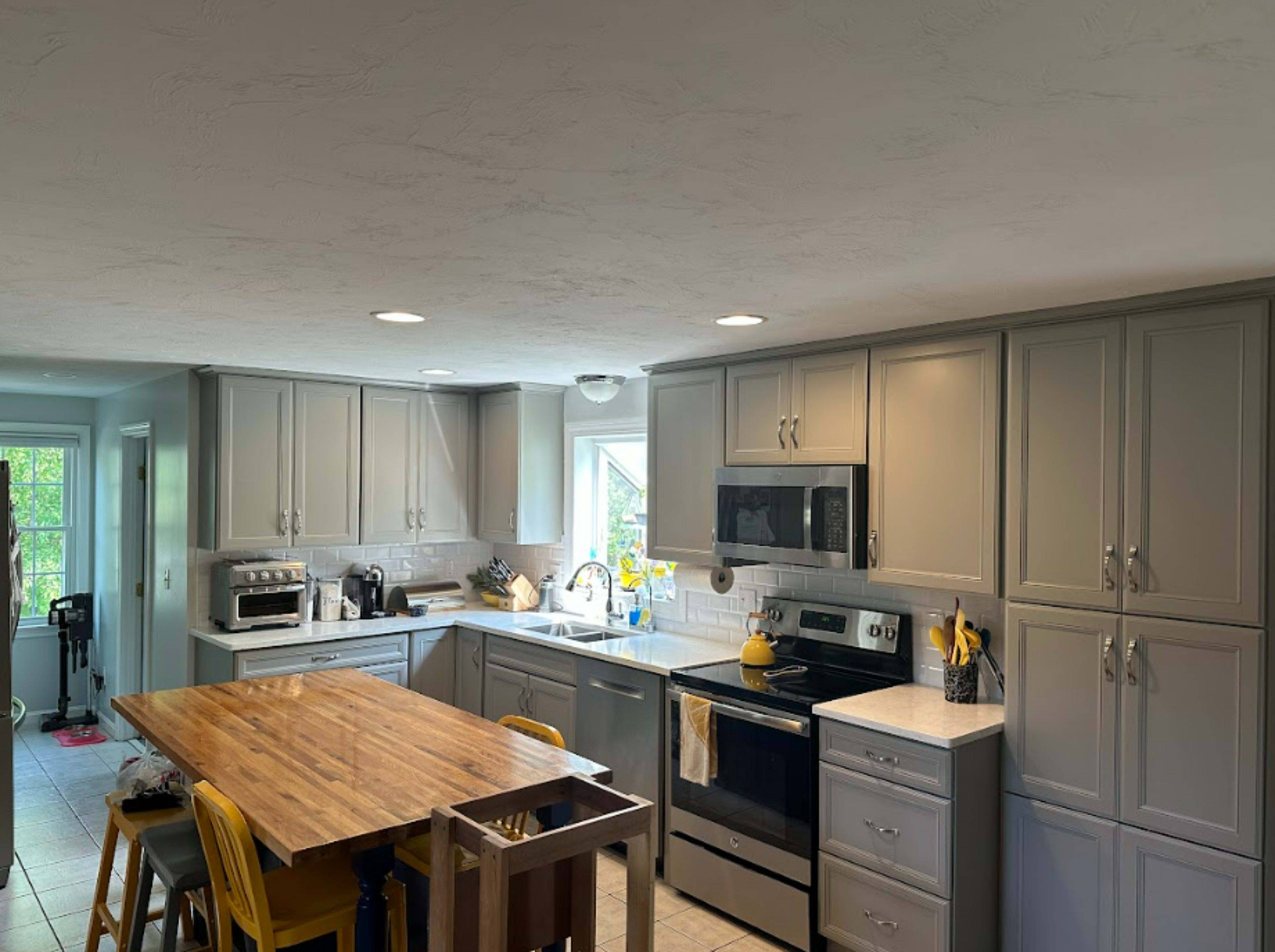 A modern kitchen features gray cabinets, stainless steel appliances, and a wooden dining table at the center.