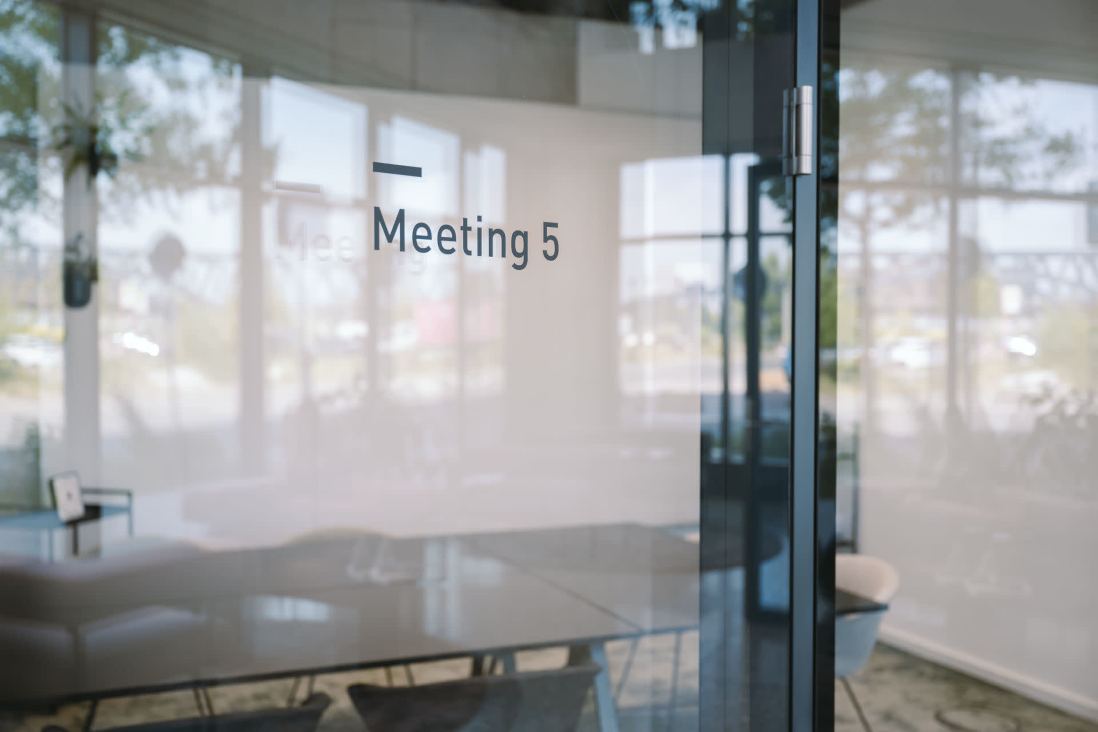 The image shows a glass door with the label "Meeting 5" indicating a conference room.
