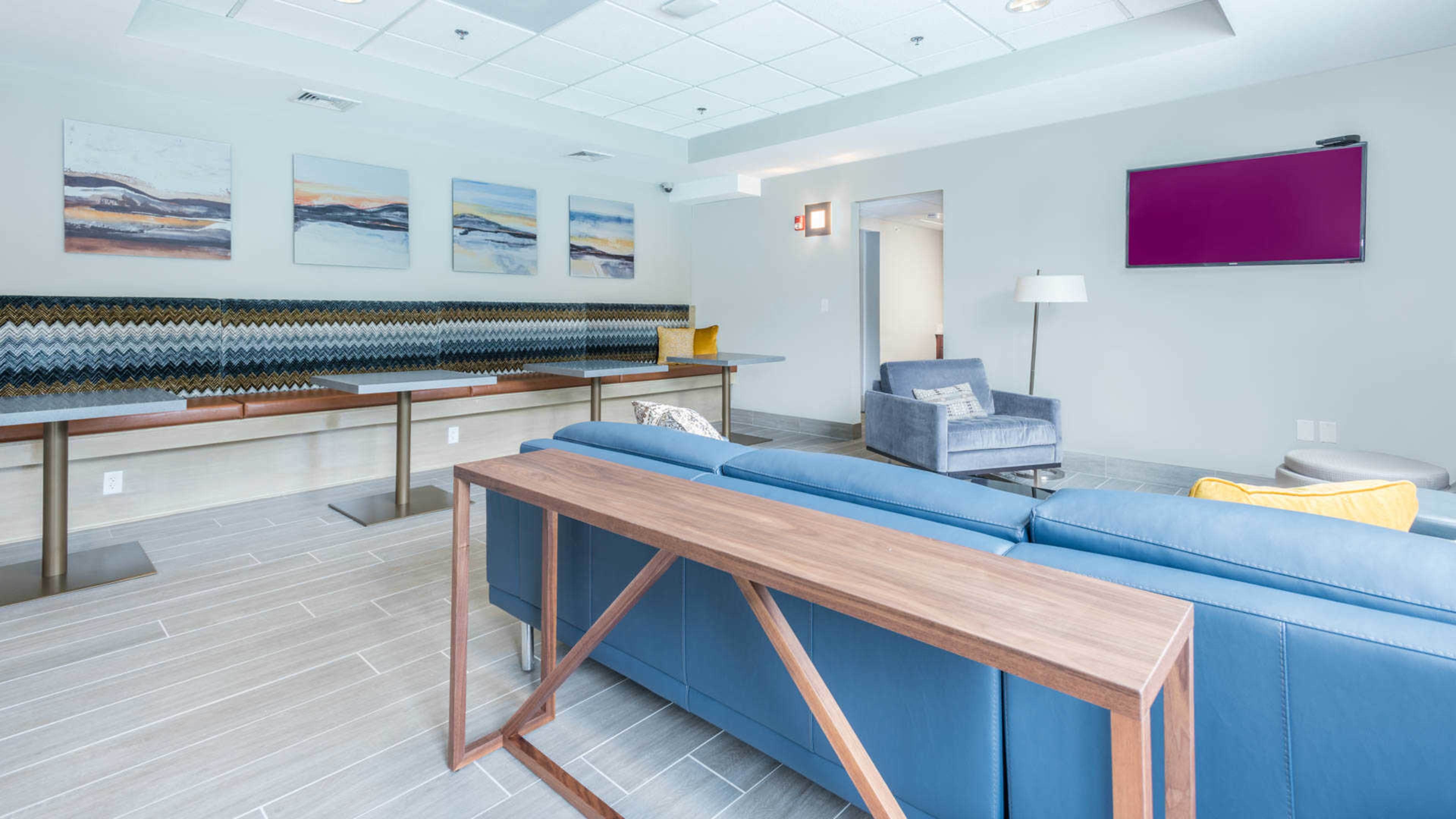A modern lounge area with a blue sofa, a wooden table, an armchair, and abstract wall art.