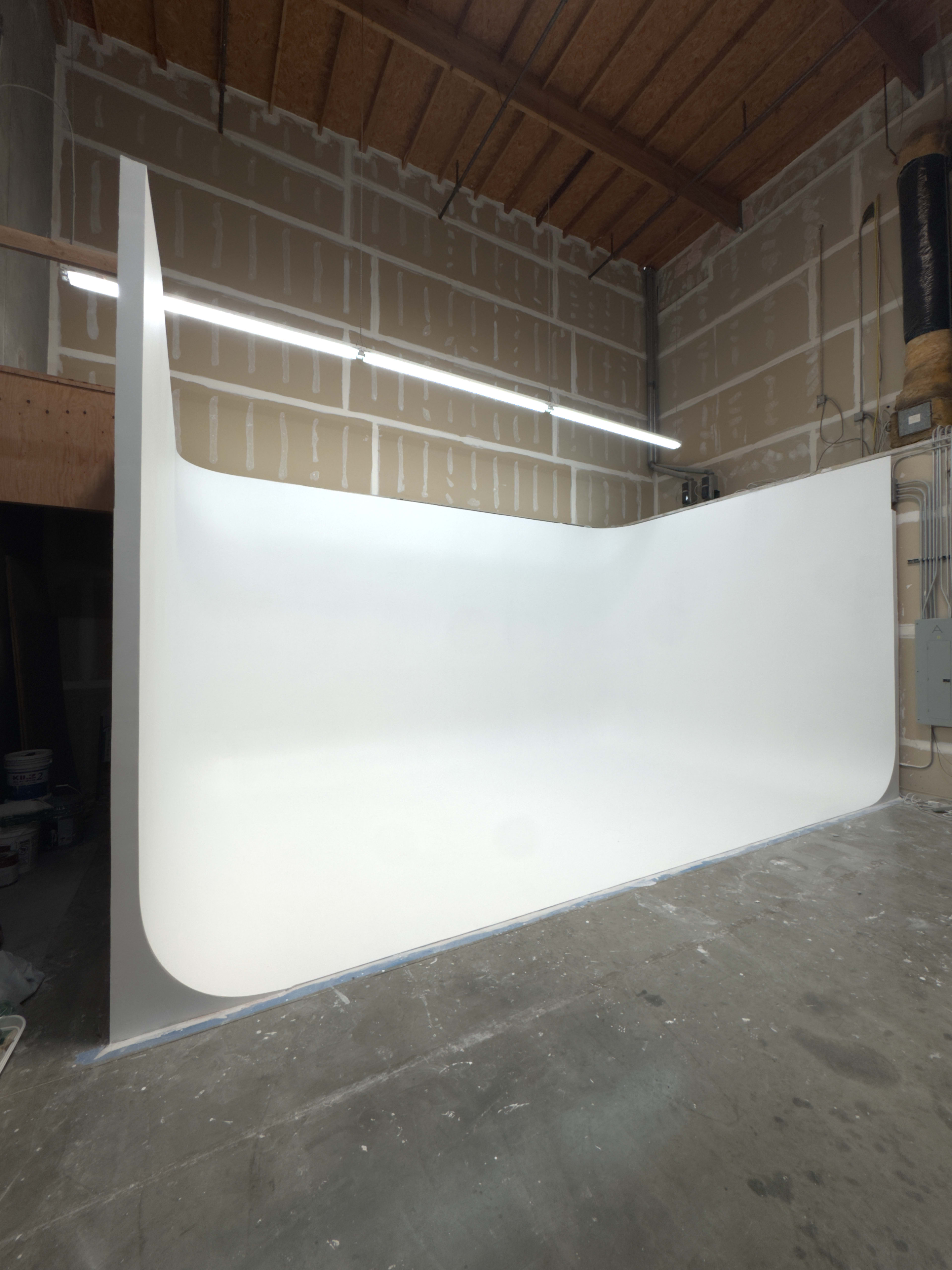 The image shows a spacious, white-walled studio or room with smooth, curved surfaces and minimal furniture.