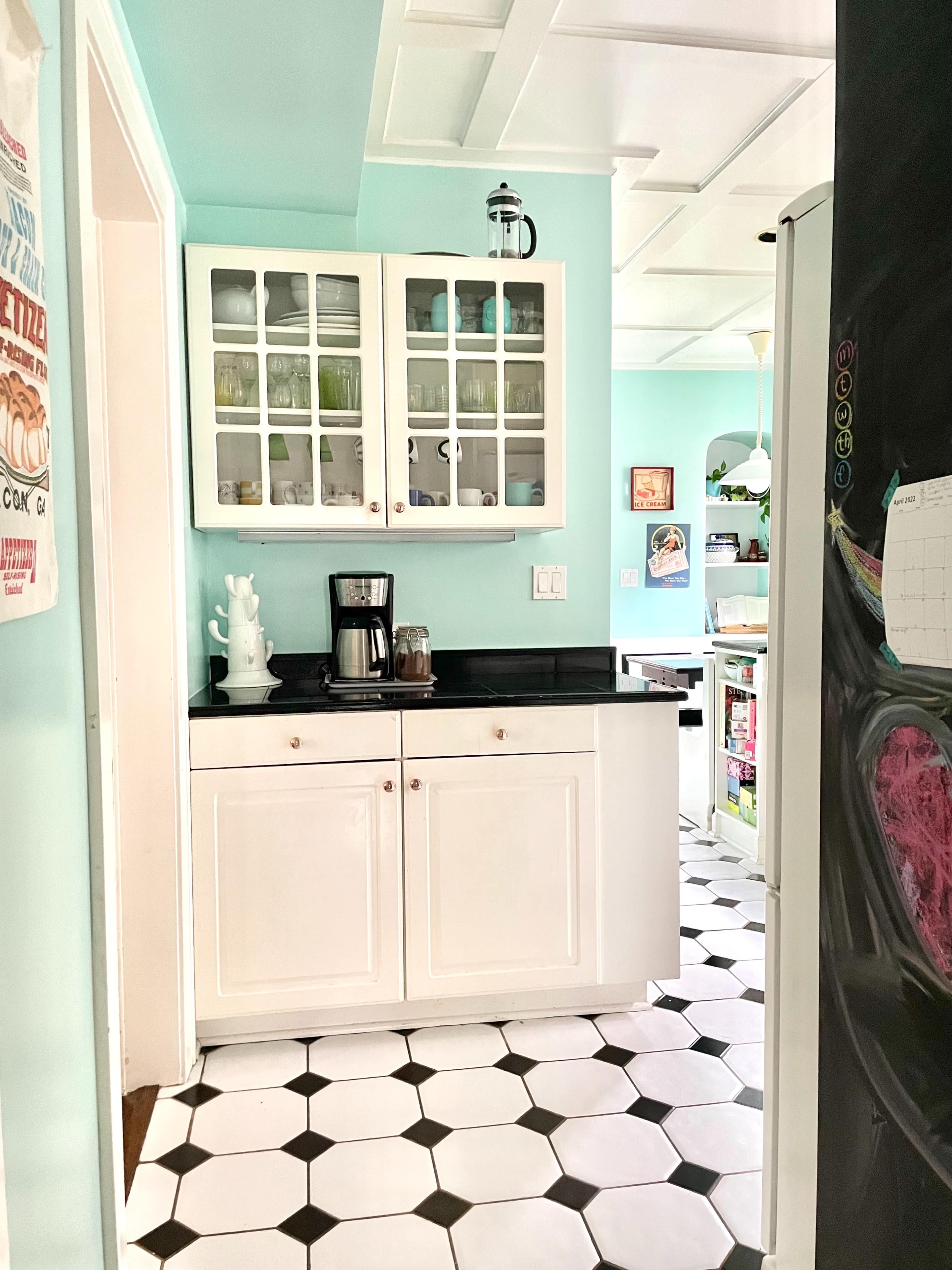 A kitchen with light blue walls, black countertops, white cabinetry with glass doors, and a checkered black and white floor.
