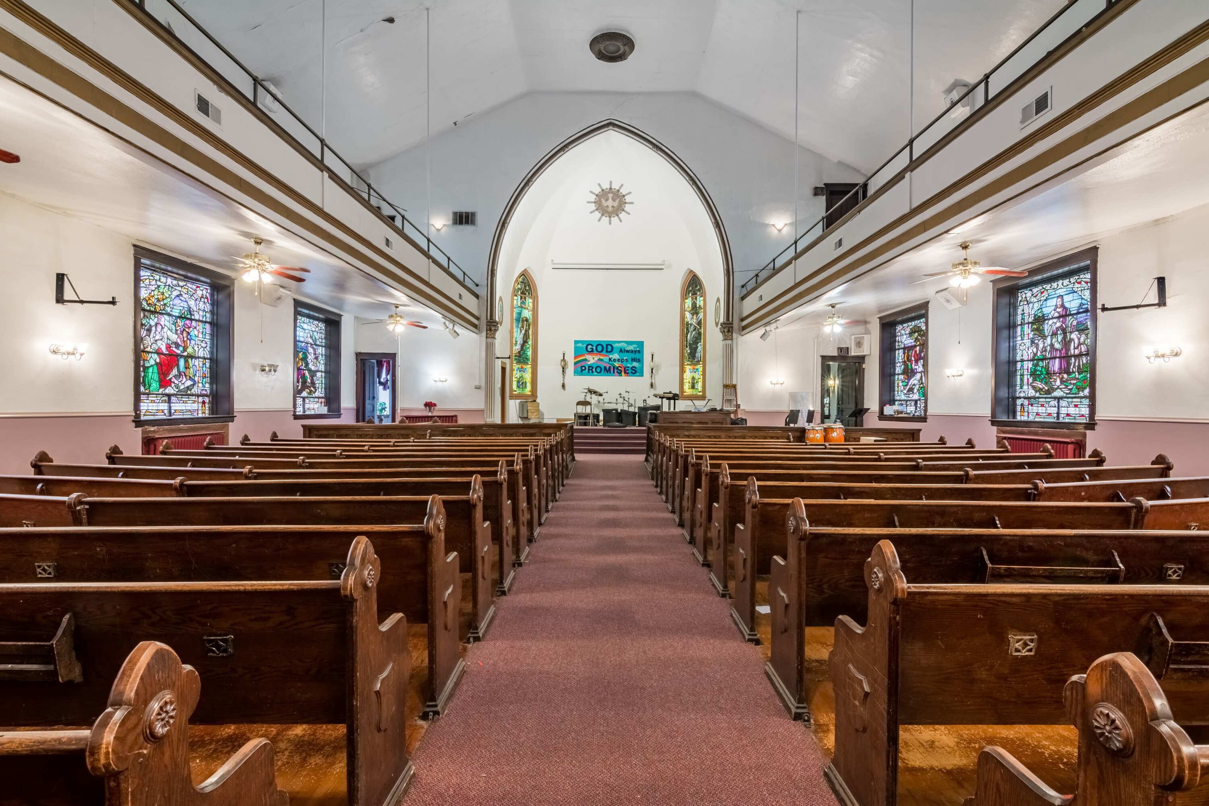 The interior of a church features wooden pews arranged in rows, with stained glass windows and a stage area at the front.