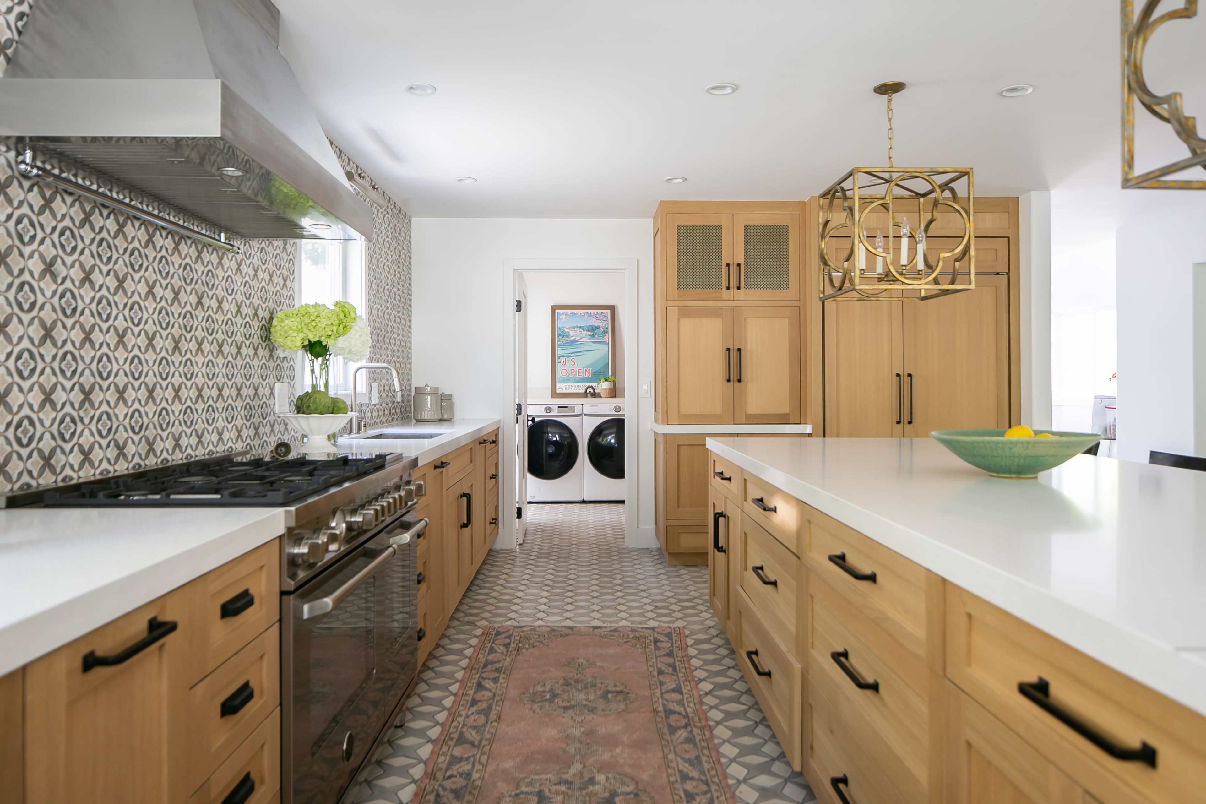 The kitchen features wooden cabinetry, a large stove, and a central island with a light fixture, complemented by a patterned backsplash and a view into a laundry area.