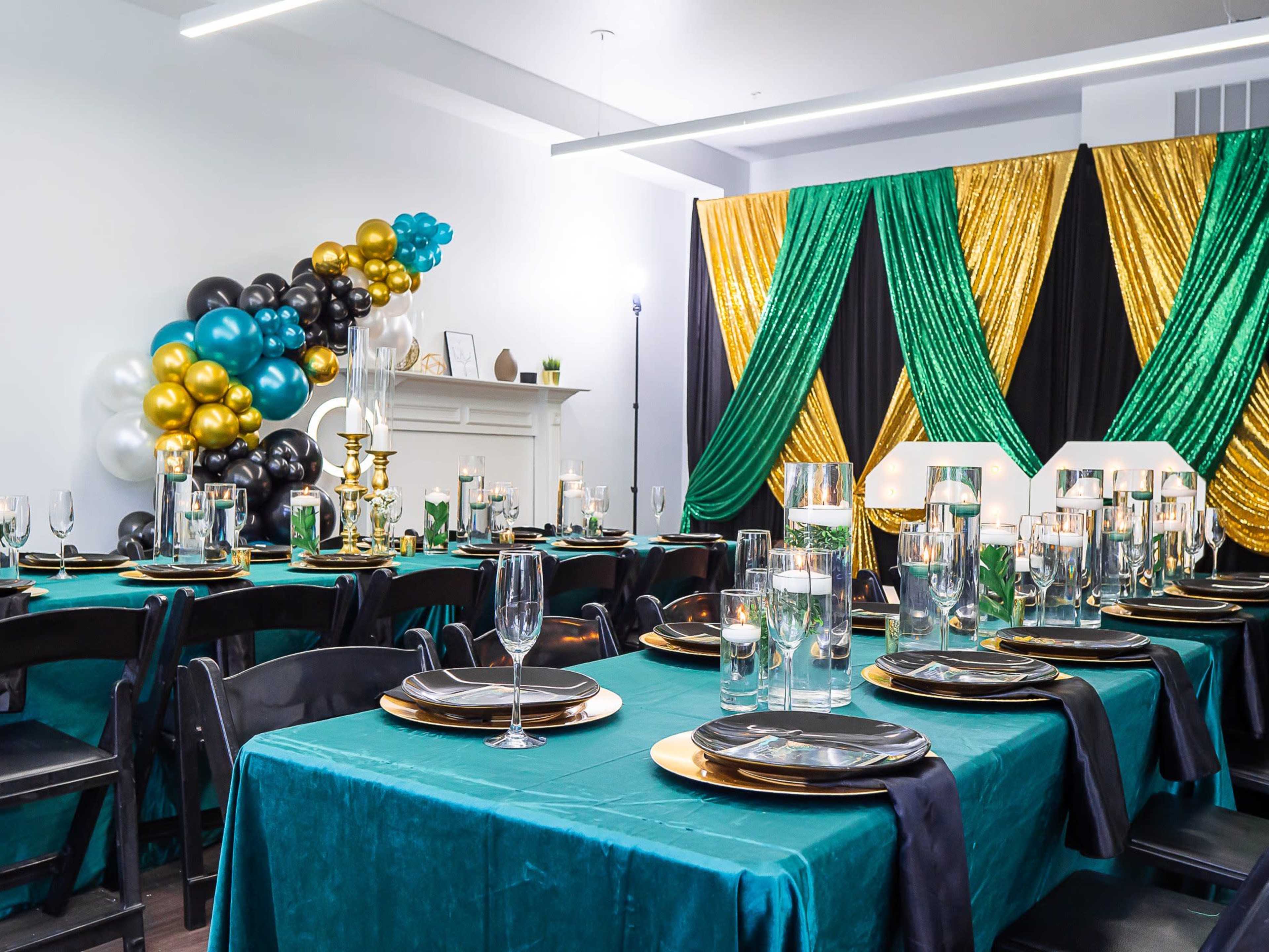 The image shows an elegantly decorated banquet hall featuring tables covered with teal cloths, gold accents, and black and gold balloons in the background.