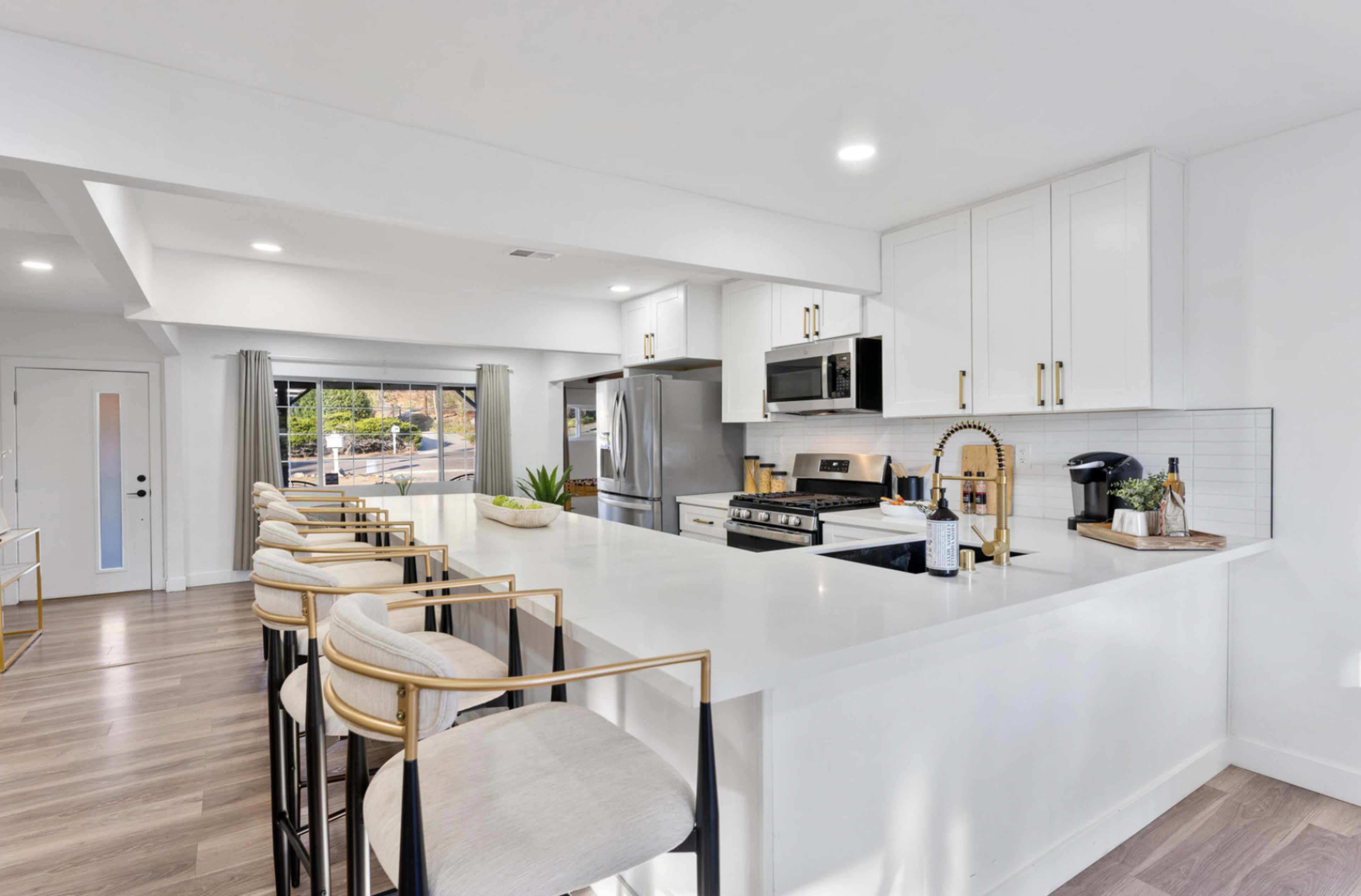 The image shows a modern kitchen with white cabinets, stainless steel appliances, and a large island with bar stools.