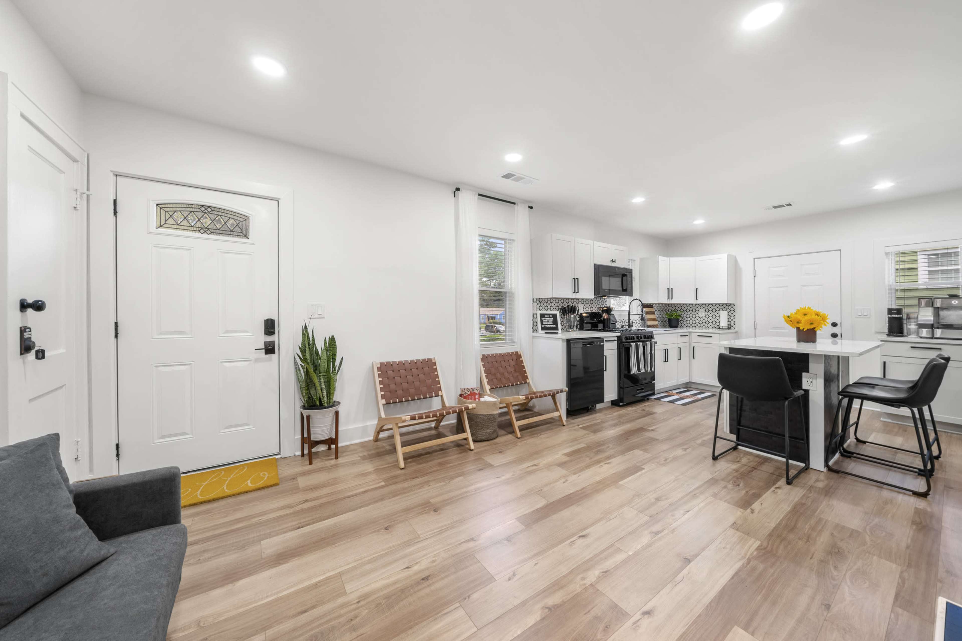 A modern open-concept living space features a kitchen and living area with wooden flooring, two chairs, and a small dining table.