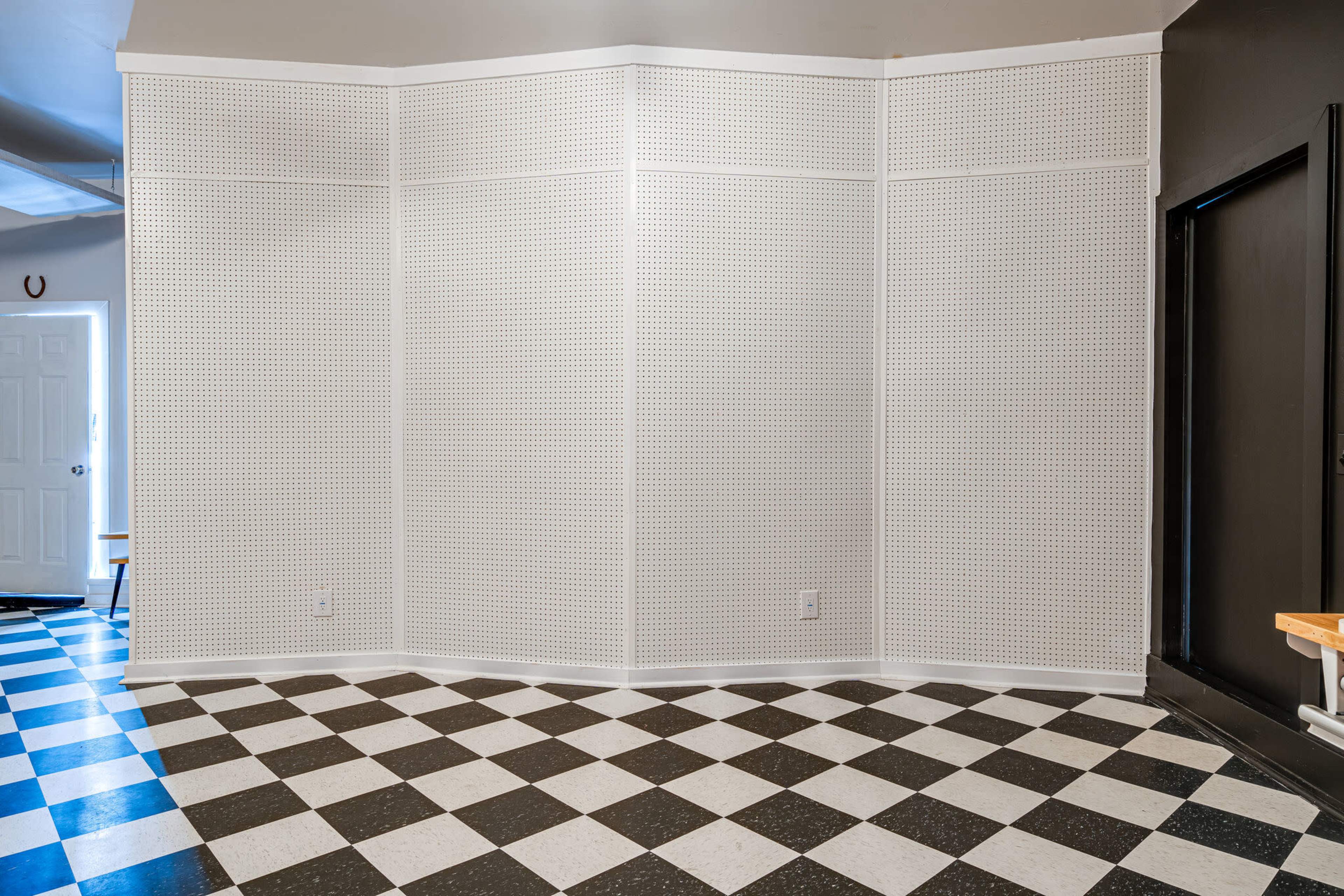 A room with a checkered black and white floor and a large, perforated white wall in the center.