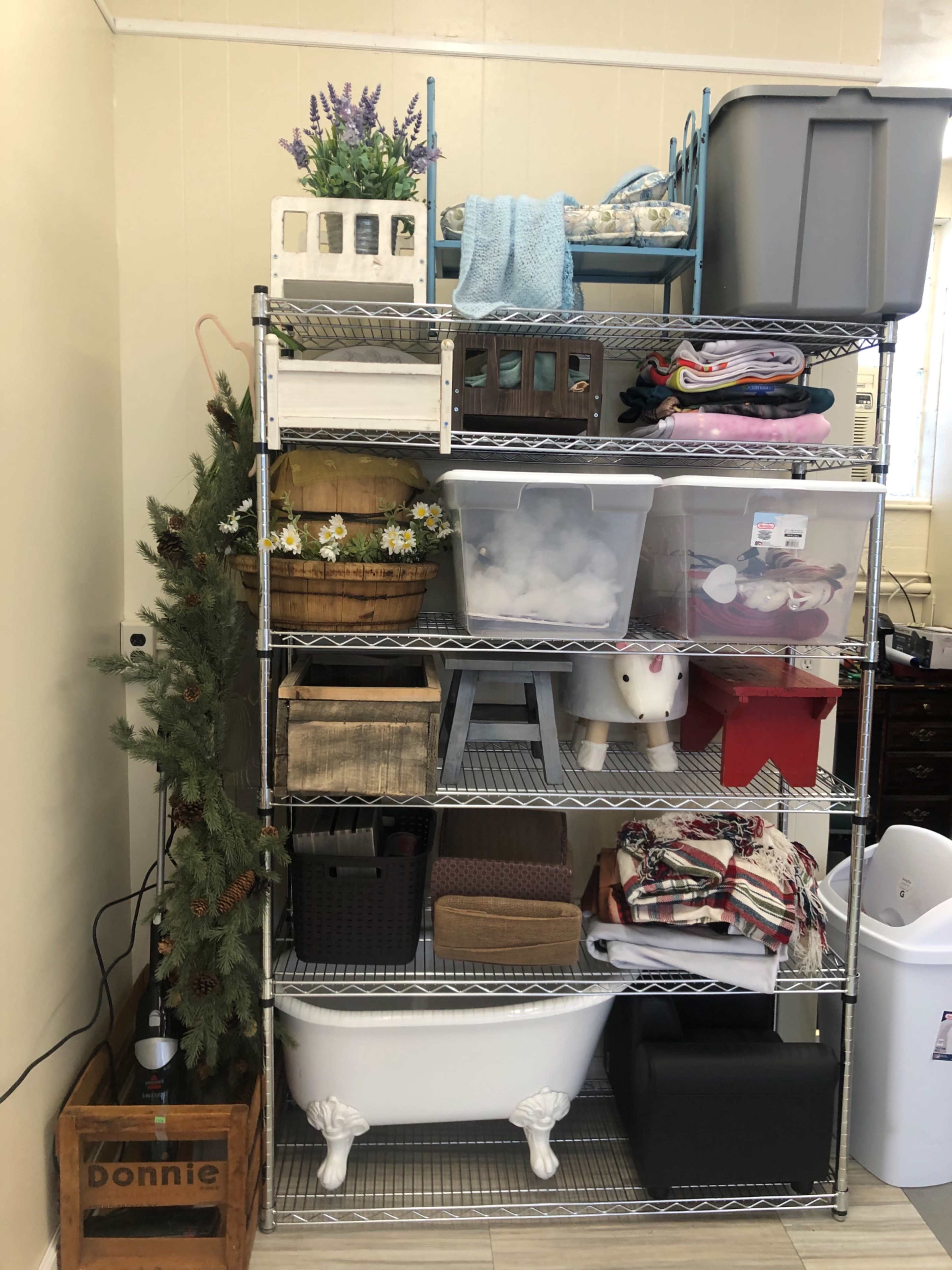 A metal shelving unit filled with various containers, baskets, and home decor items, alongside a small artificial Christmas tree.