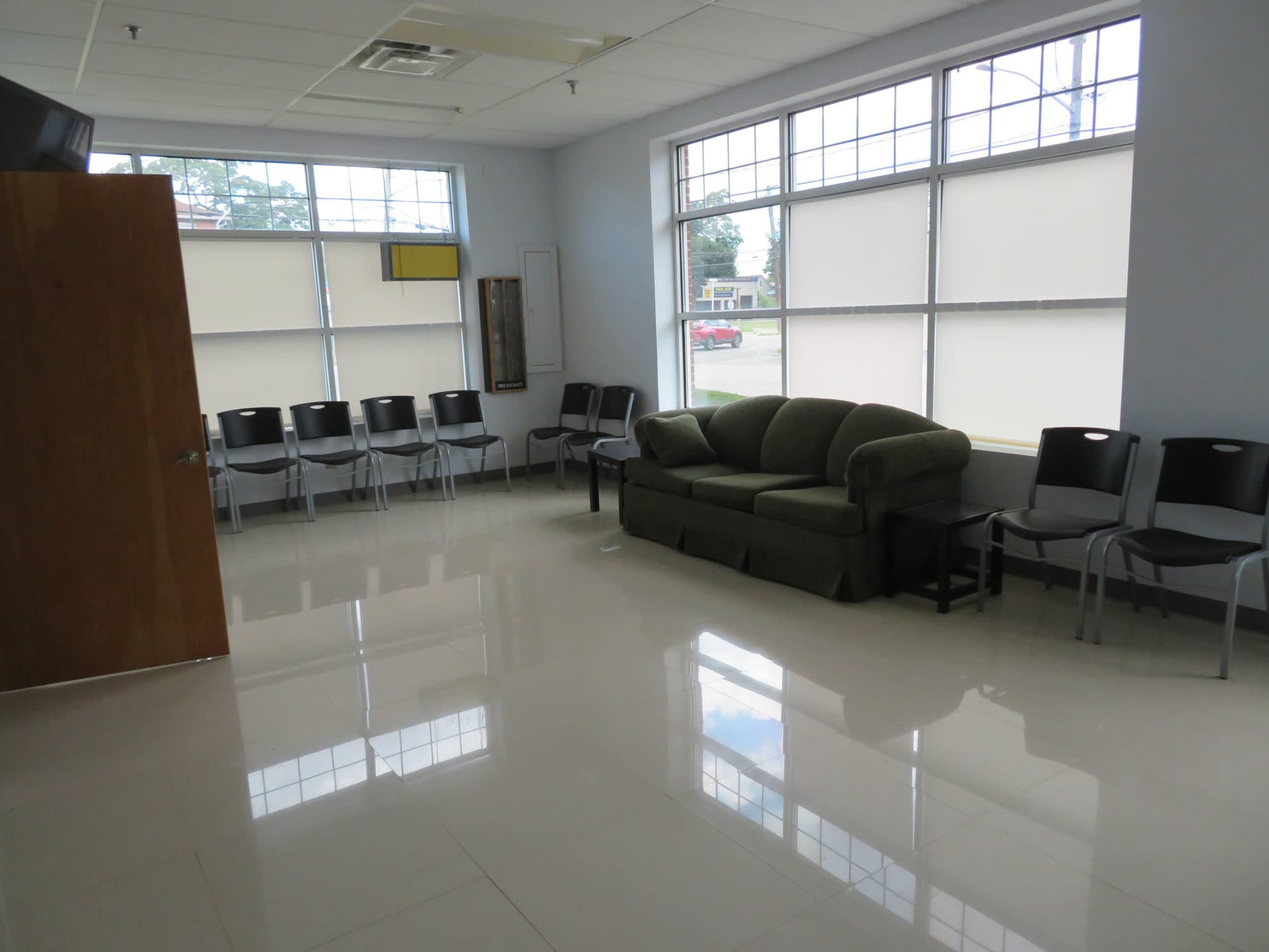 The image shows a quiet waiting room with a green couch and several metal chairs near large windows.