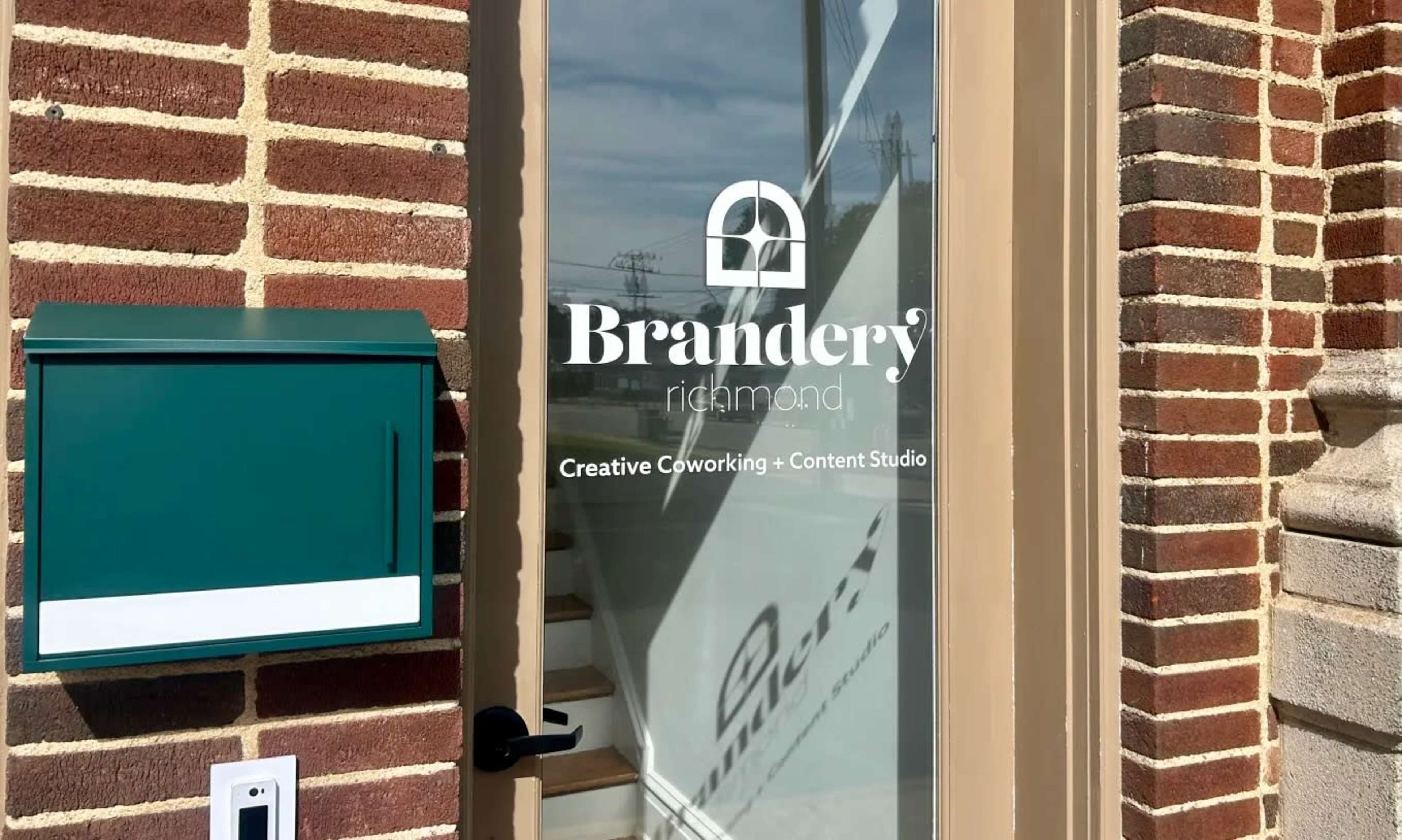 The image shows a glass door with a logo for "Brandery" and a green mail box attached beside it.